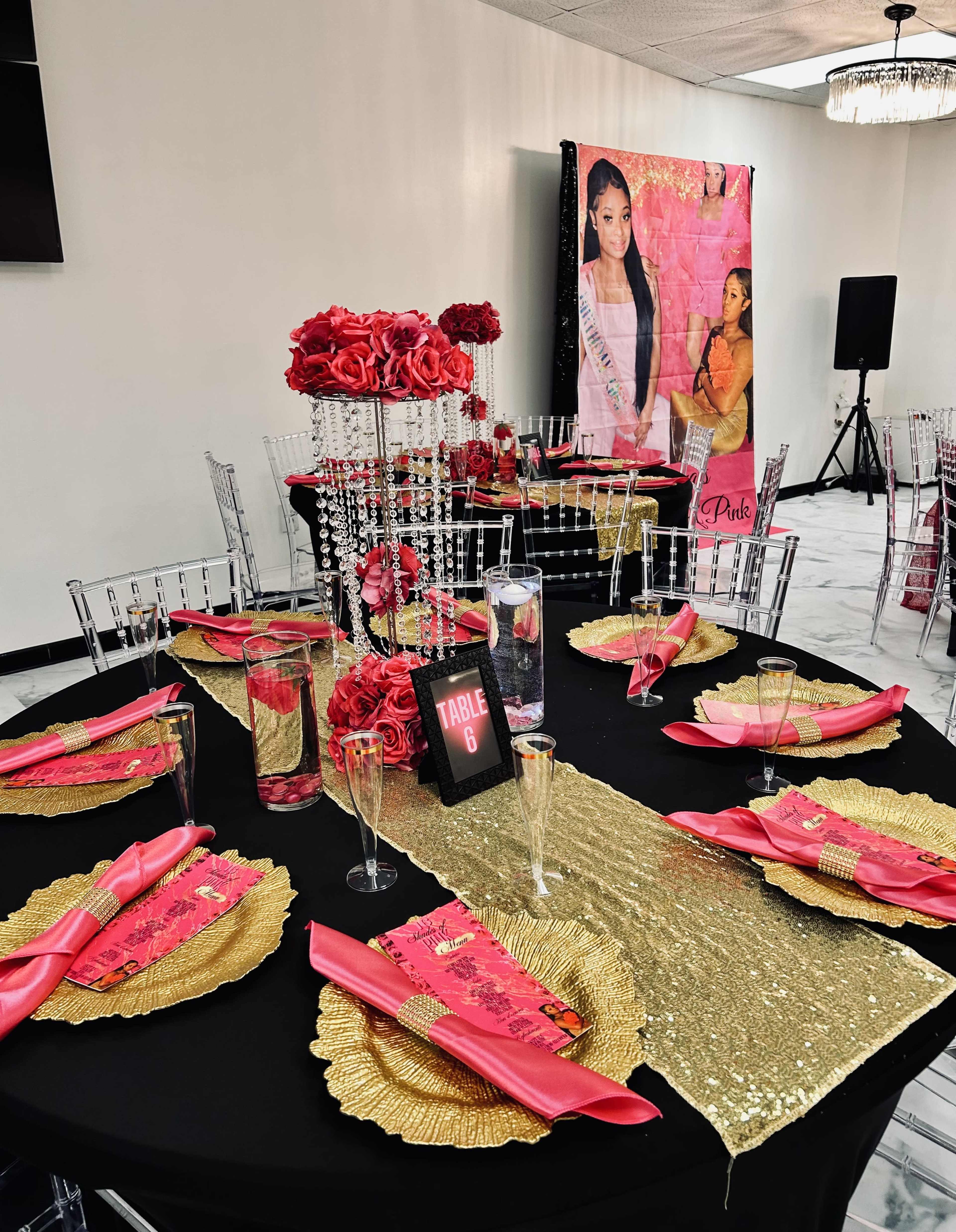 The image shows a banquet setup with a black tablecloth, gold and pink accents, and decorative floral arrangements, arranged for a formal event.