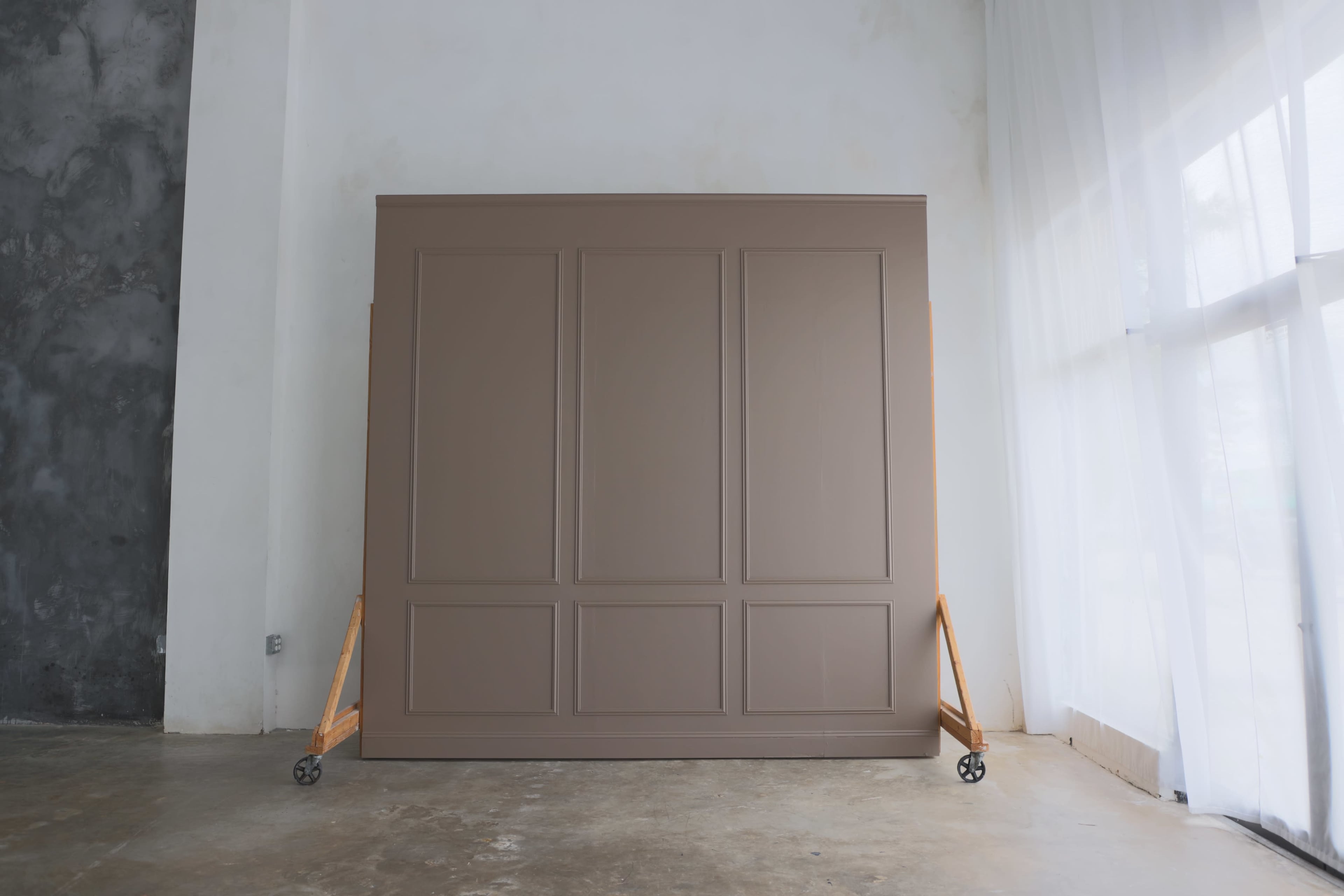 A large, featureless brown panel stands against a white wall with a wooden support on each side.