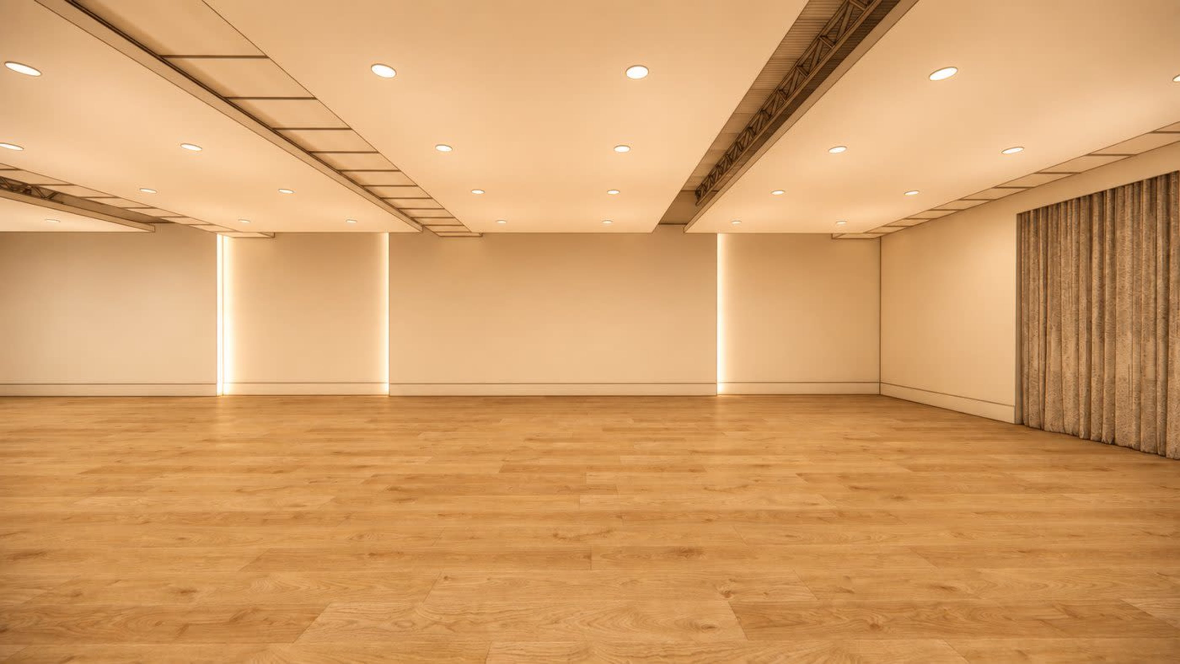 The image shows a spacious interior room with wooden flooring, illuminated by recessed lighting and featuring plain walls.