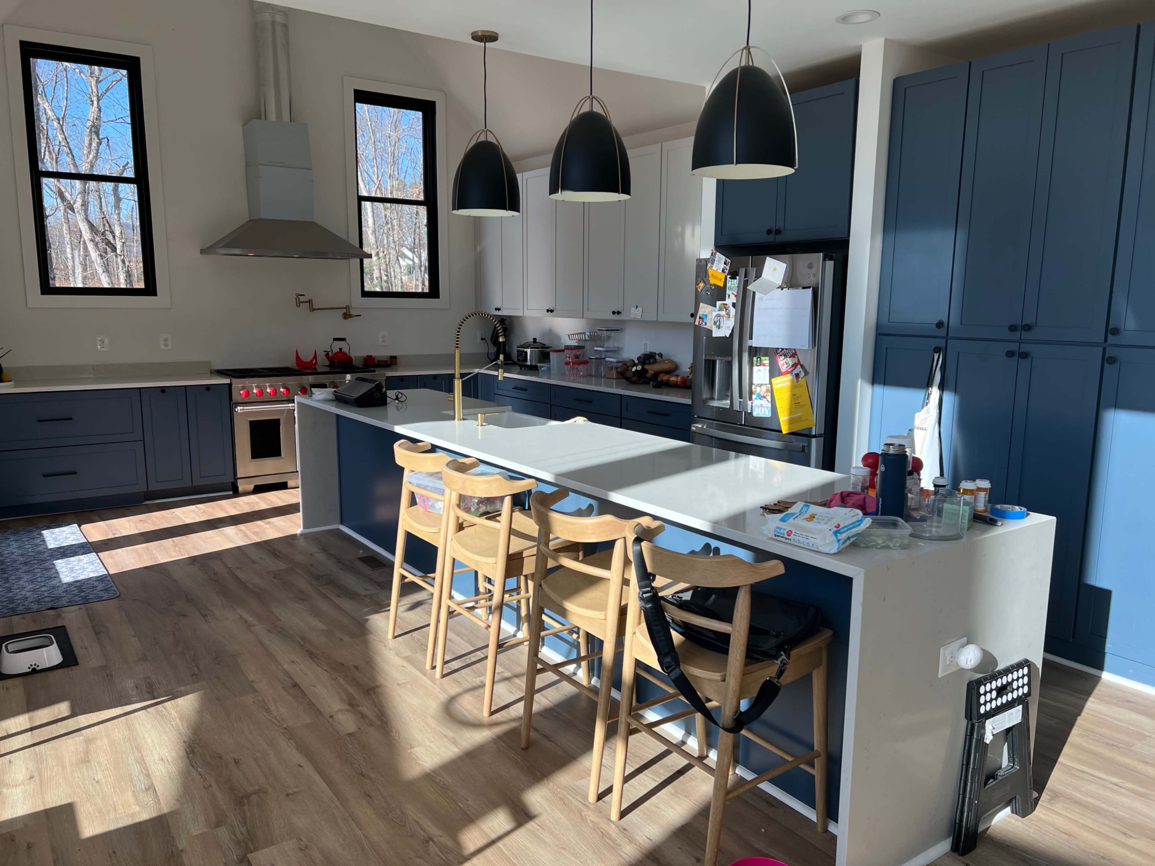 The kitchen features a long island with barstools, dual-tone cabinets, and pendant lights hanging above.