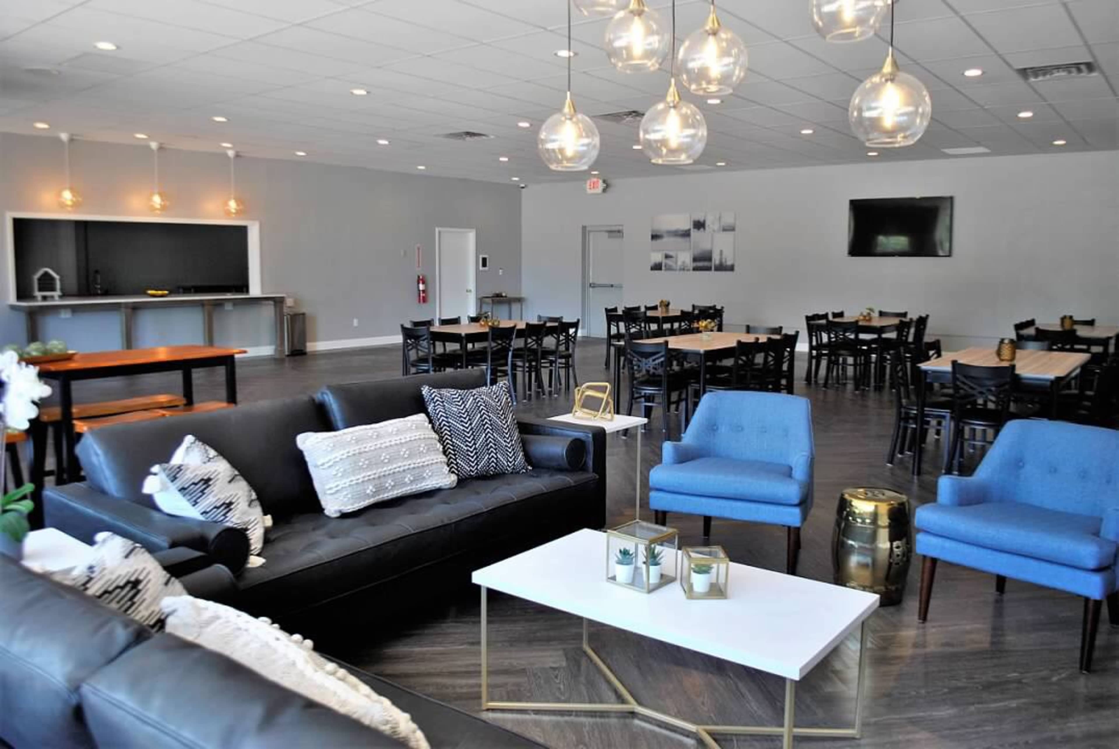 A spacious, modern event room with a seating area featuring a black sofa and blue chairs, alongside tables arranged for dining.