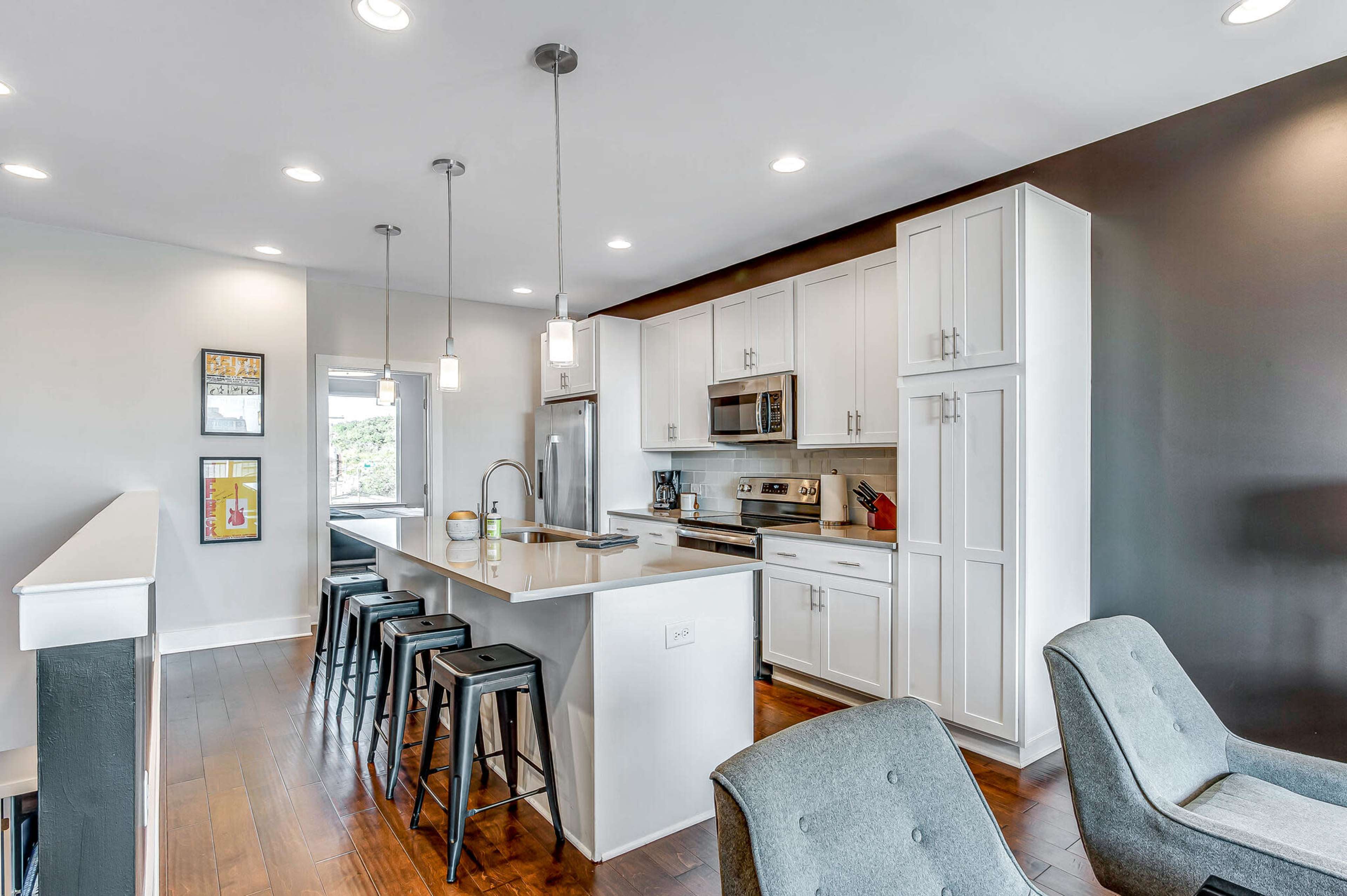 The image features a modern kitchen with white cabinetry, stainless steel appliances, a central island with bar stools, and hardwood flooring.