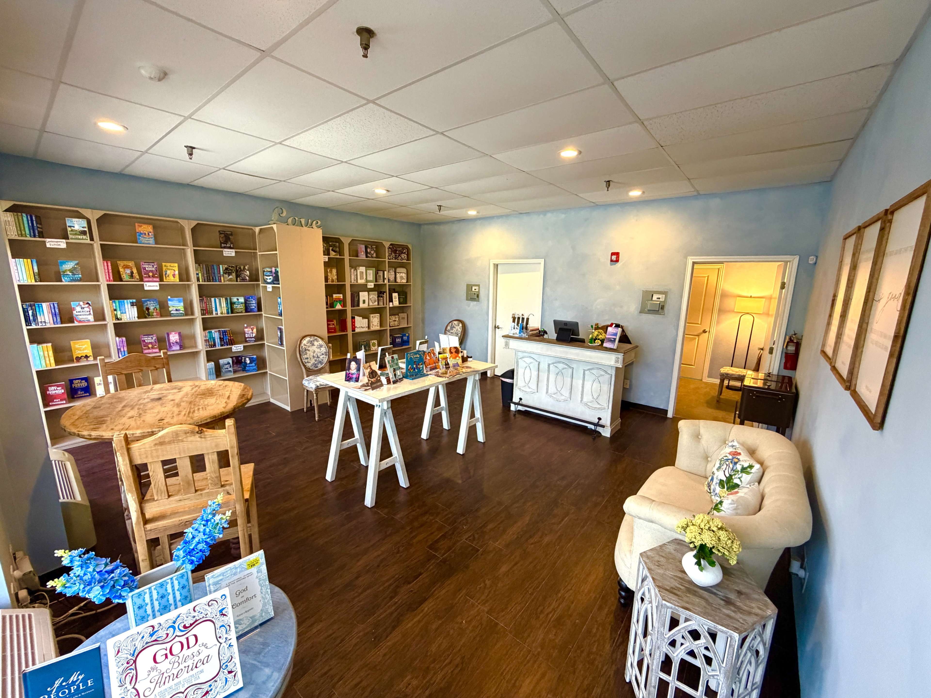 The image shows an inviting office space with bookshelves filled with various books, a reception desk, a small seating area, and decorative elements throughout.