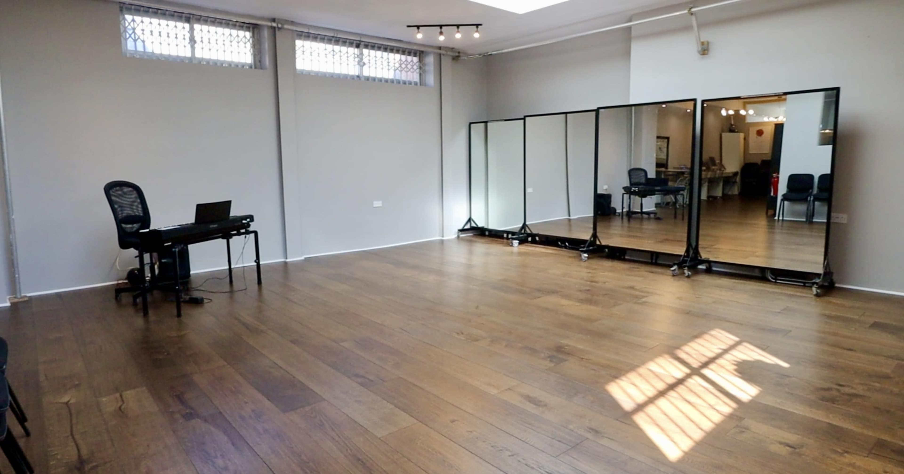 A spacious room with wooden floors, a desk and chair set up on one side, and a row of large mirrors along the opposite wall.