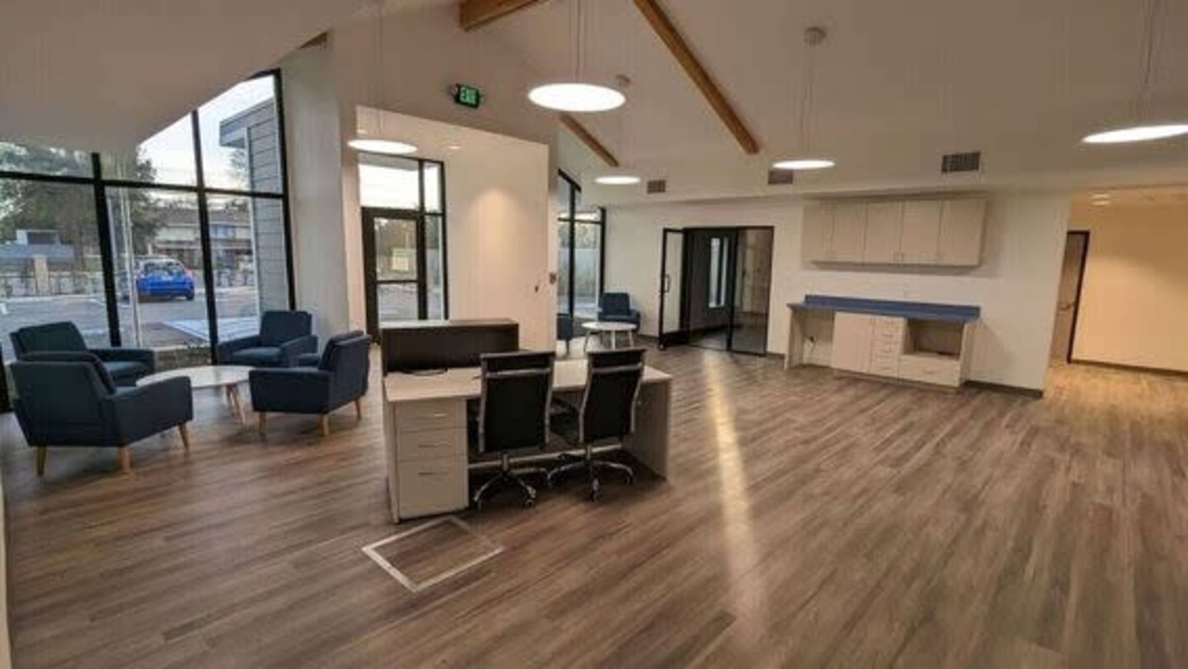 A modern, spacious office interior with a seating area, desks, and large windows.