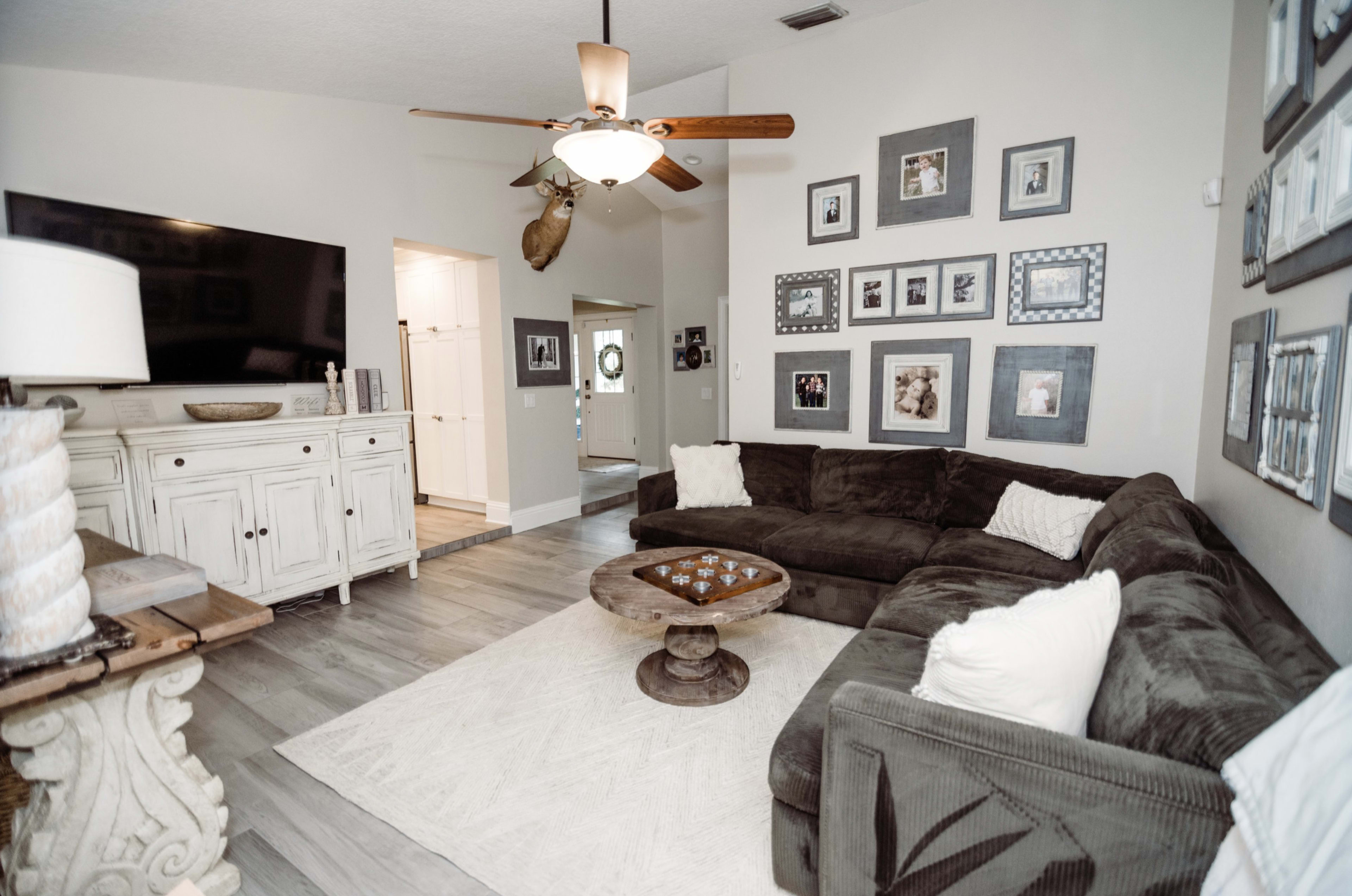 The living room features a sectional sofa, wooden coffee table, and a wall decorated with framed photos.