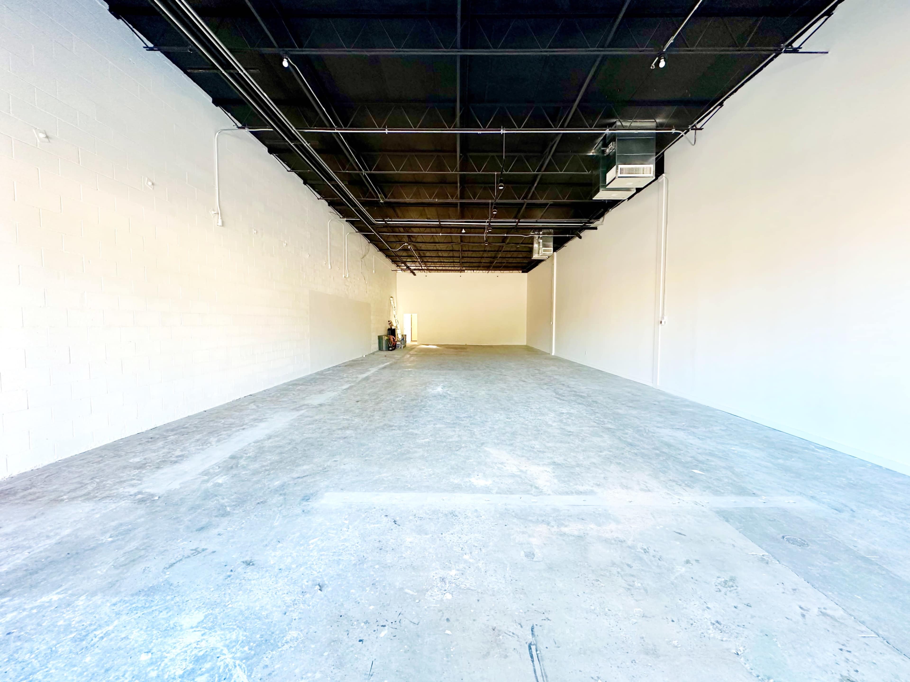 The image shows a large, empty commercial space with concrete flooring and white walls.
