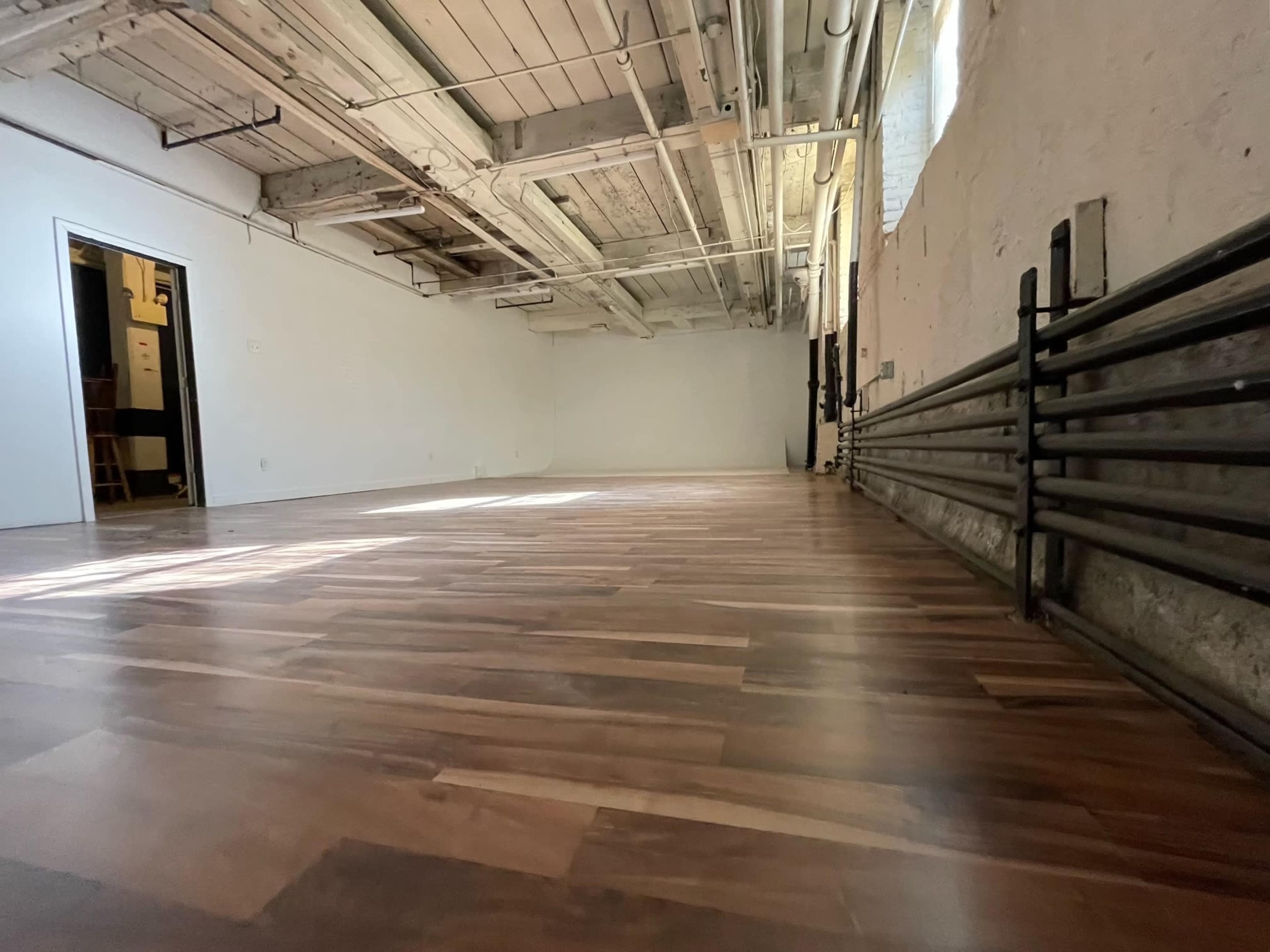 An empty room with polished wooden flooring and exposed ceiling beams.