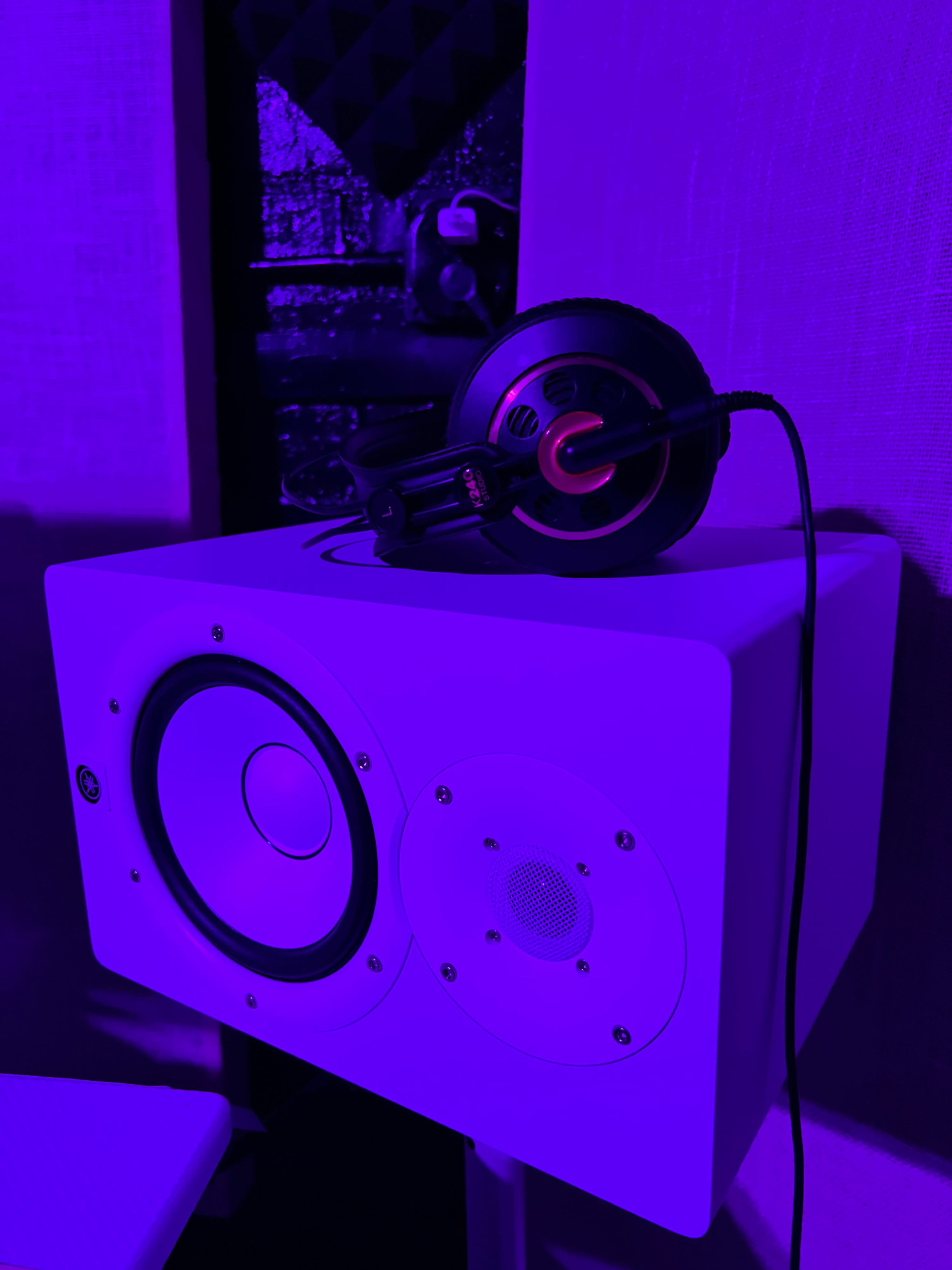 A studio monitor speaker sits on a surface with a pair of headphones resting on top.