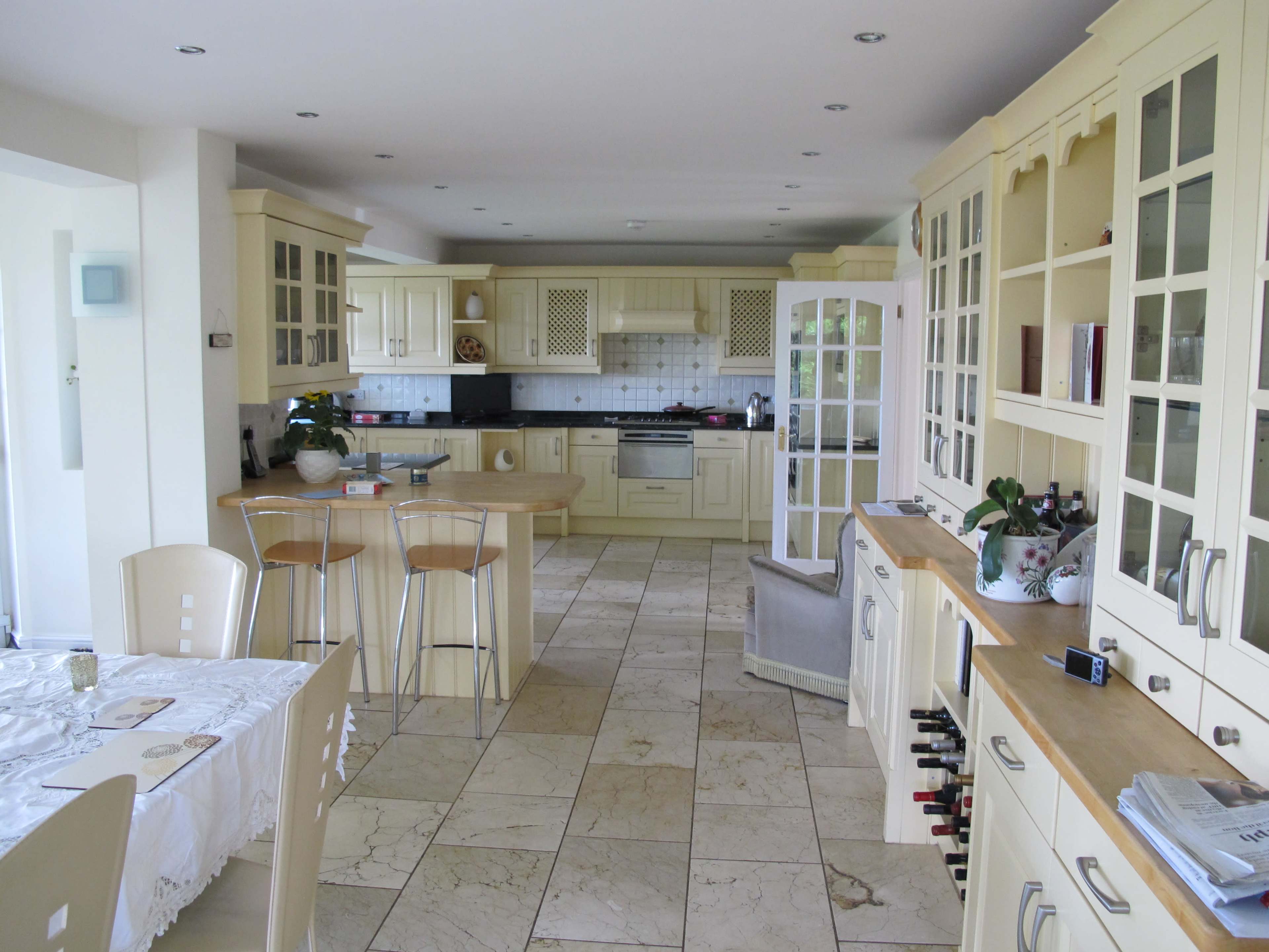 A spacious kitchen features cream-colored cabinetry, a central island with bar stools, and a tiled floor.