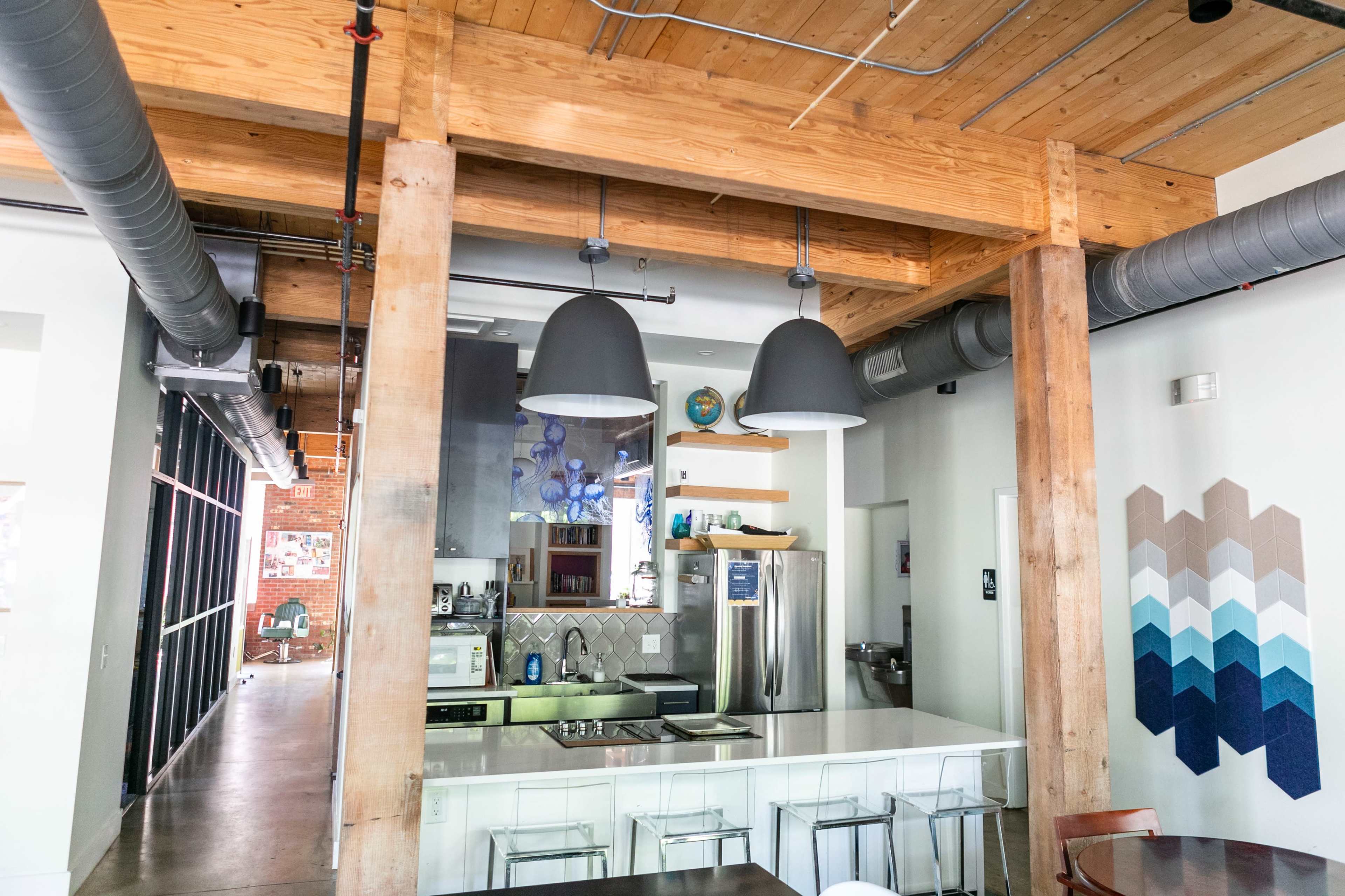 The image shows a modern kitchen area with wooden beams, an island counter, and two large pendant lights above.