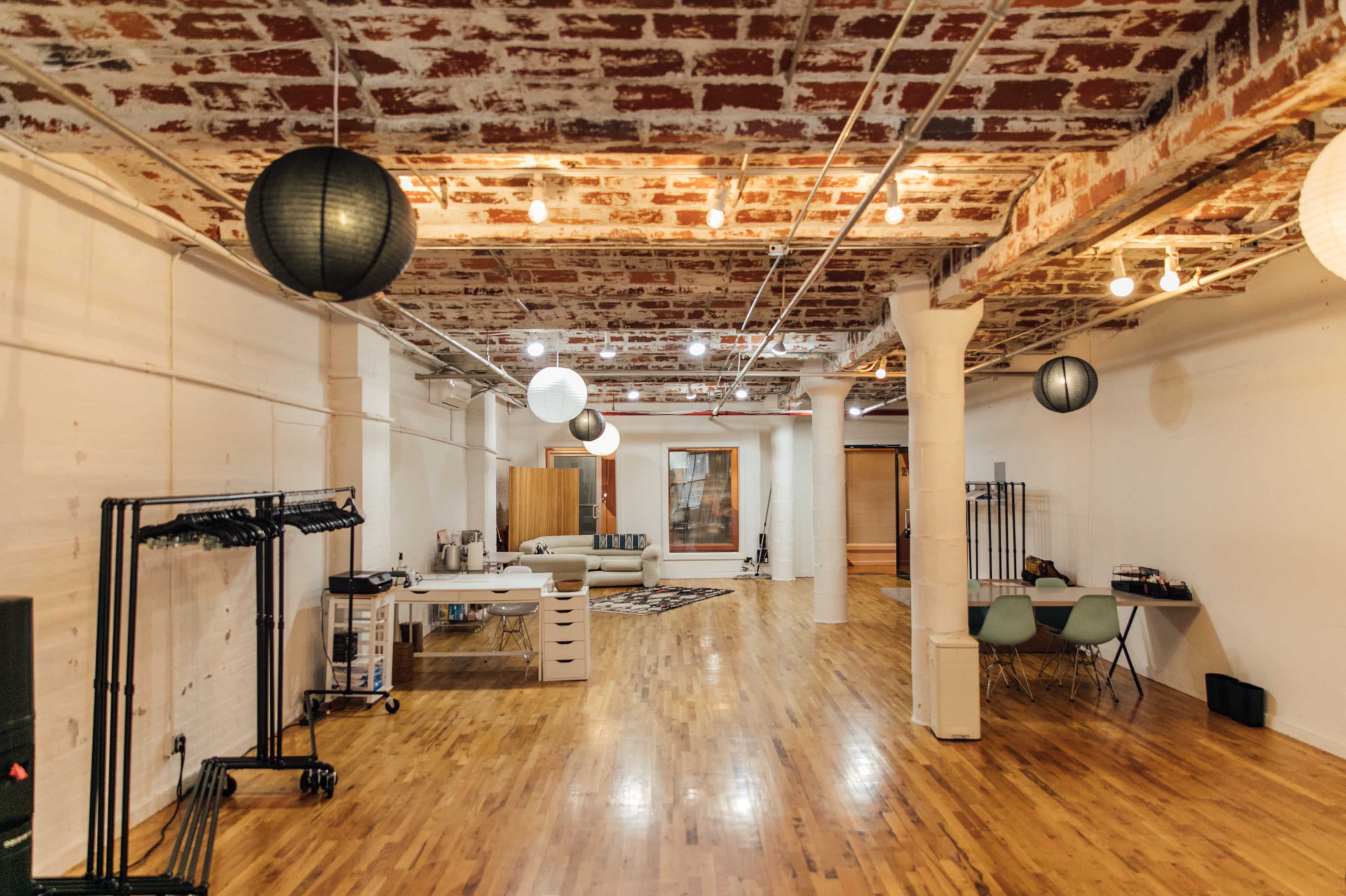 The image shows a spacious interior with exposed brick walls, wooden flooring, and various hanging lanterns, featuring furniture and equipment along the sides.