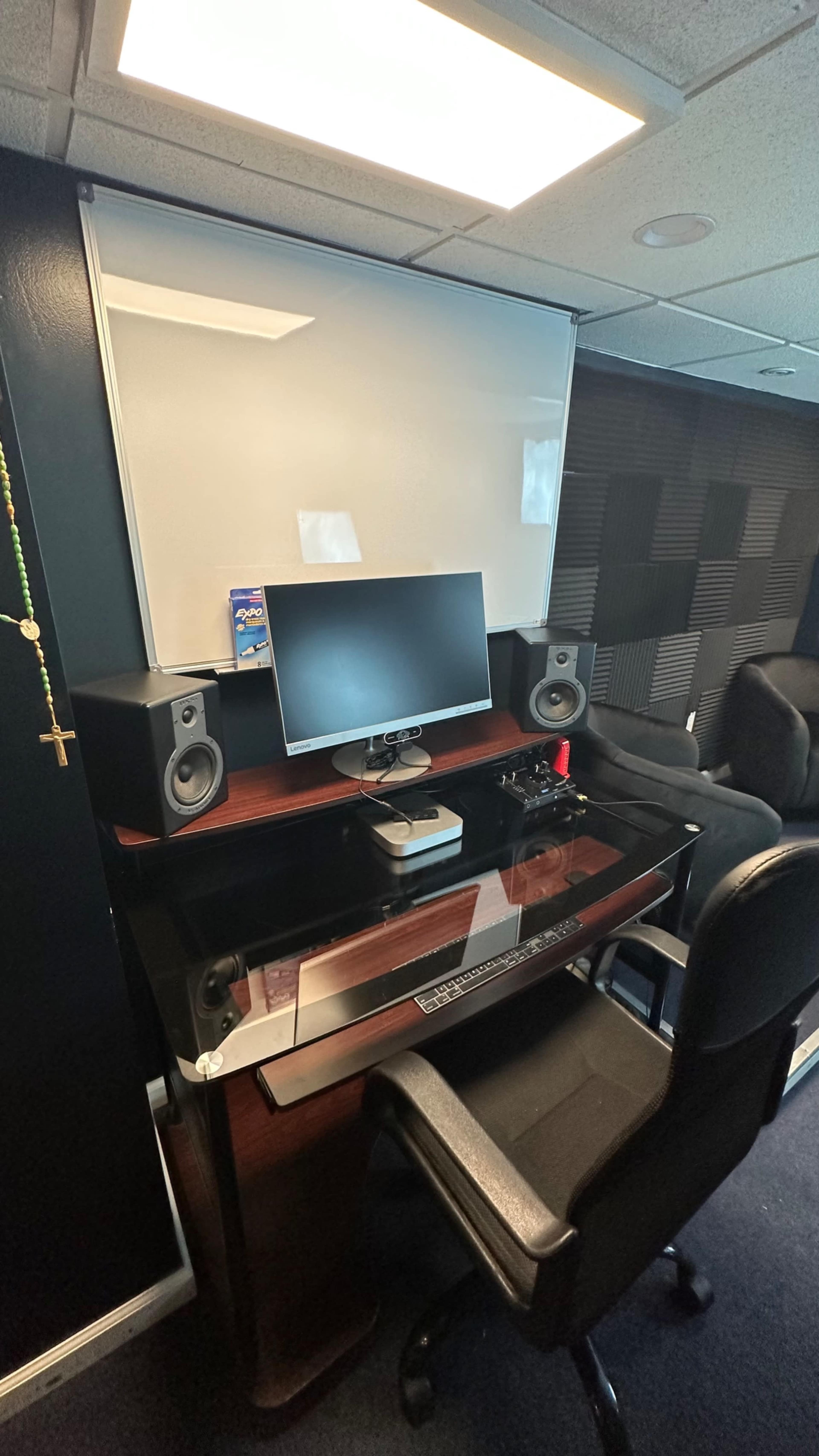 A modern office setup with a monitor, speakers, and a black ergonomic chair in front of a glass-topped desk.