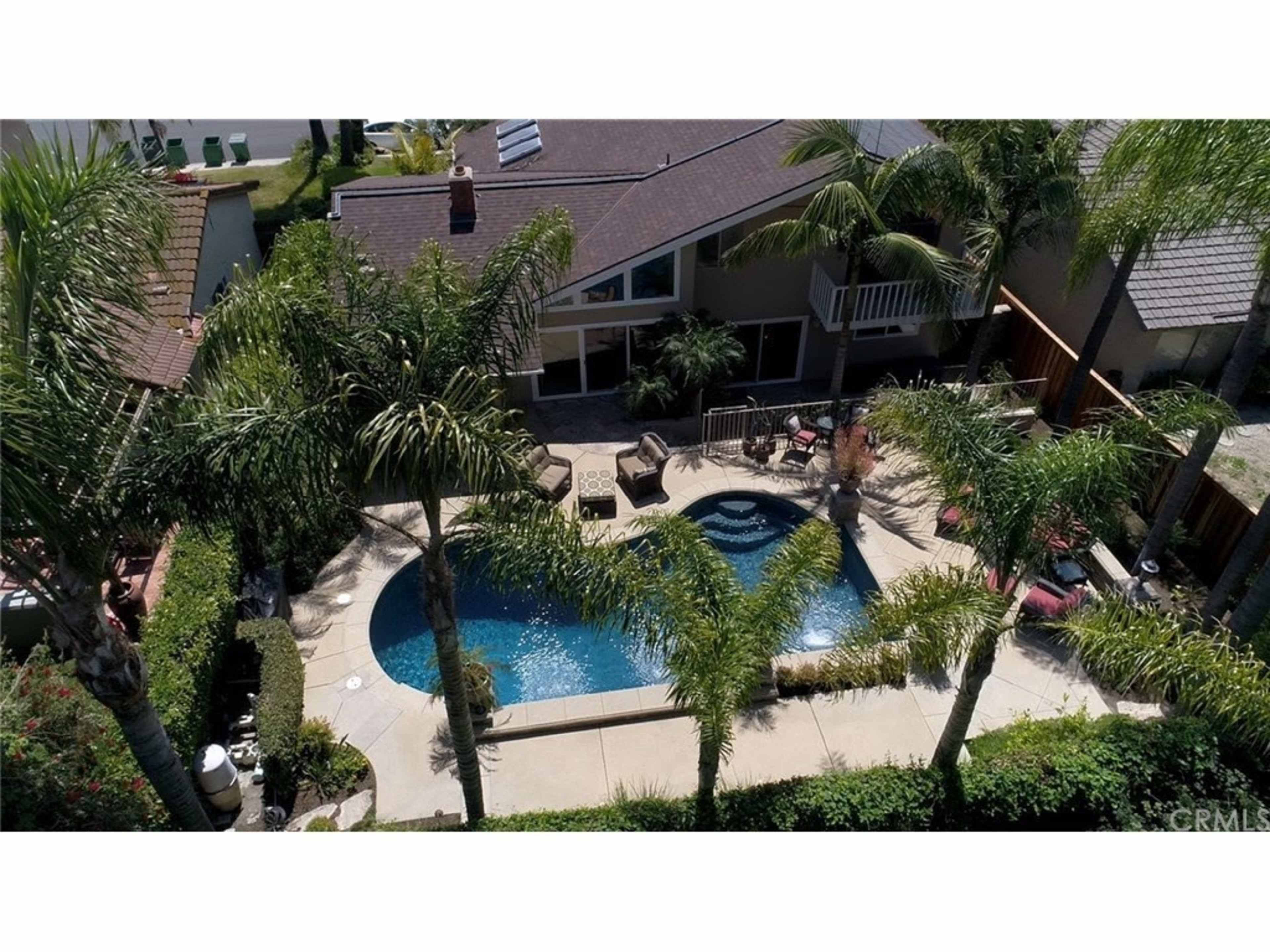 The image shows a backyard with a swimming pool surrounded by palm trees, patio furniture, and a house in the background.