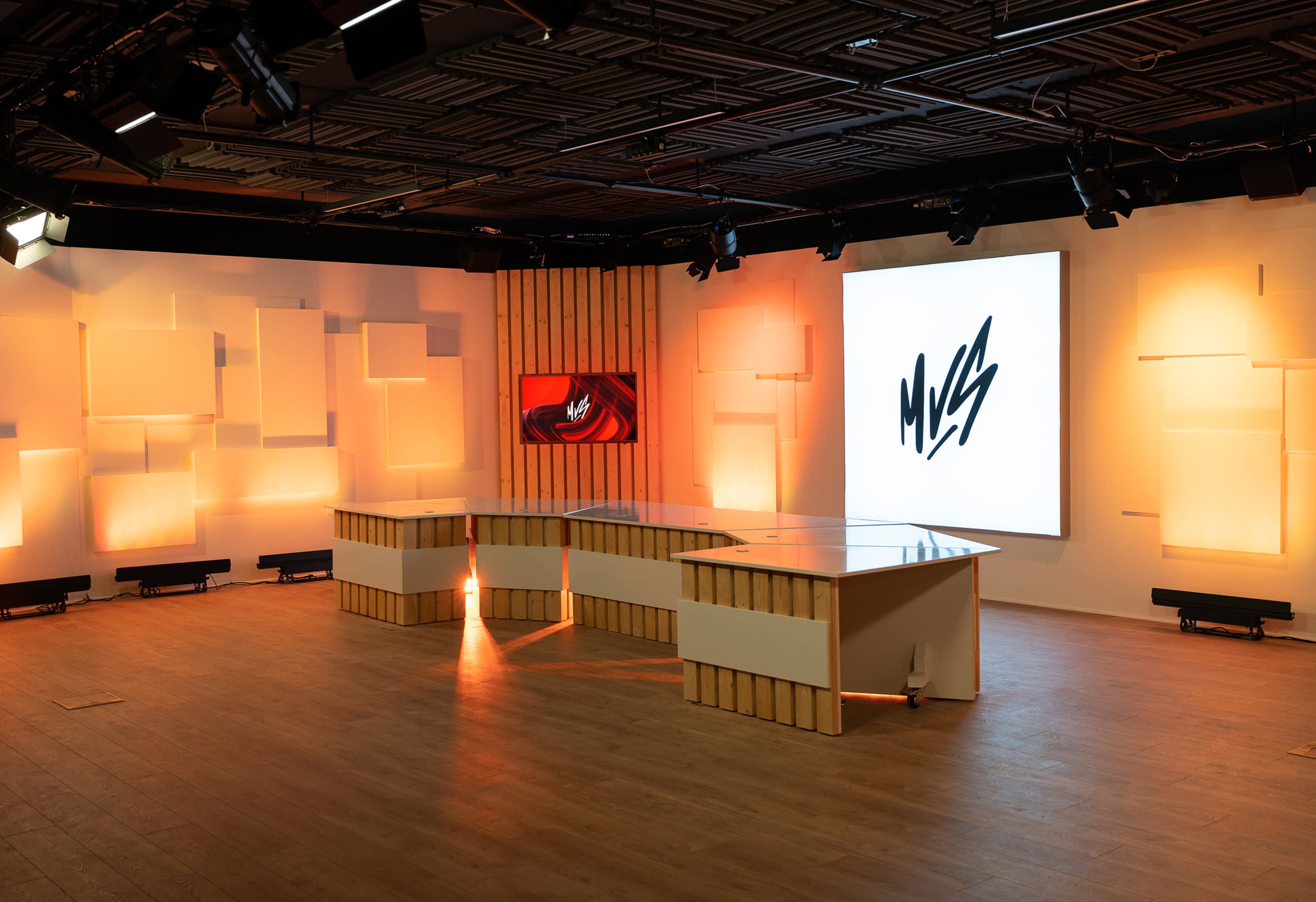 A modern studio setup with a central table and large screens displaying graphics, illuminated by soft orange lighting.
