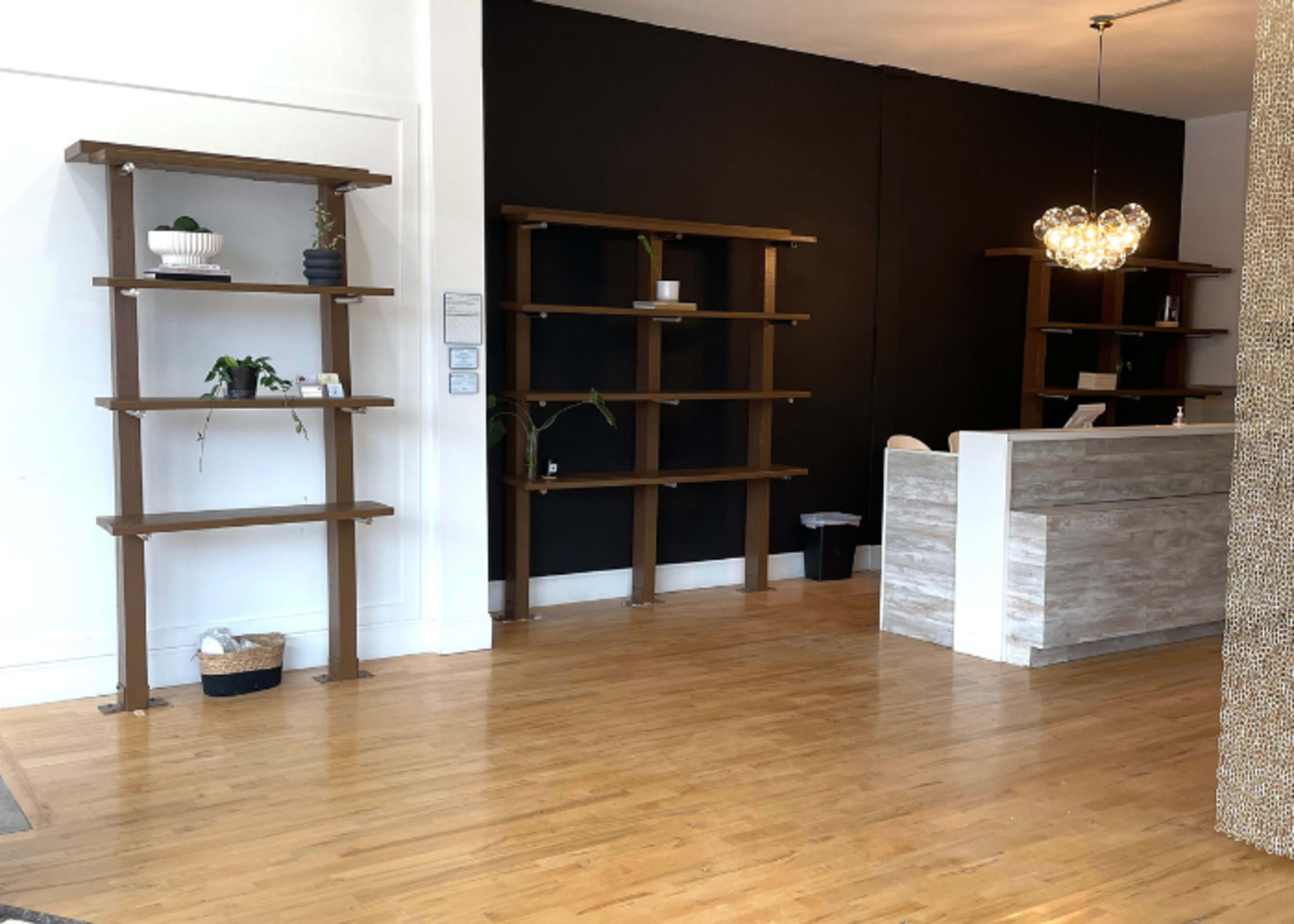 A minimalist reception area with wooden shelves on the left wall and a white reception desk against a dark wall.