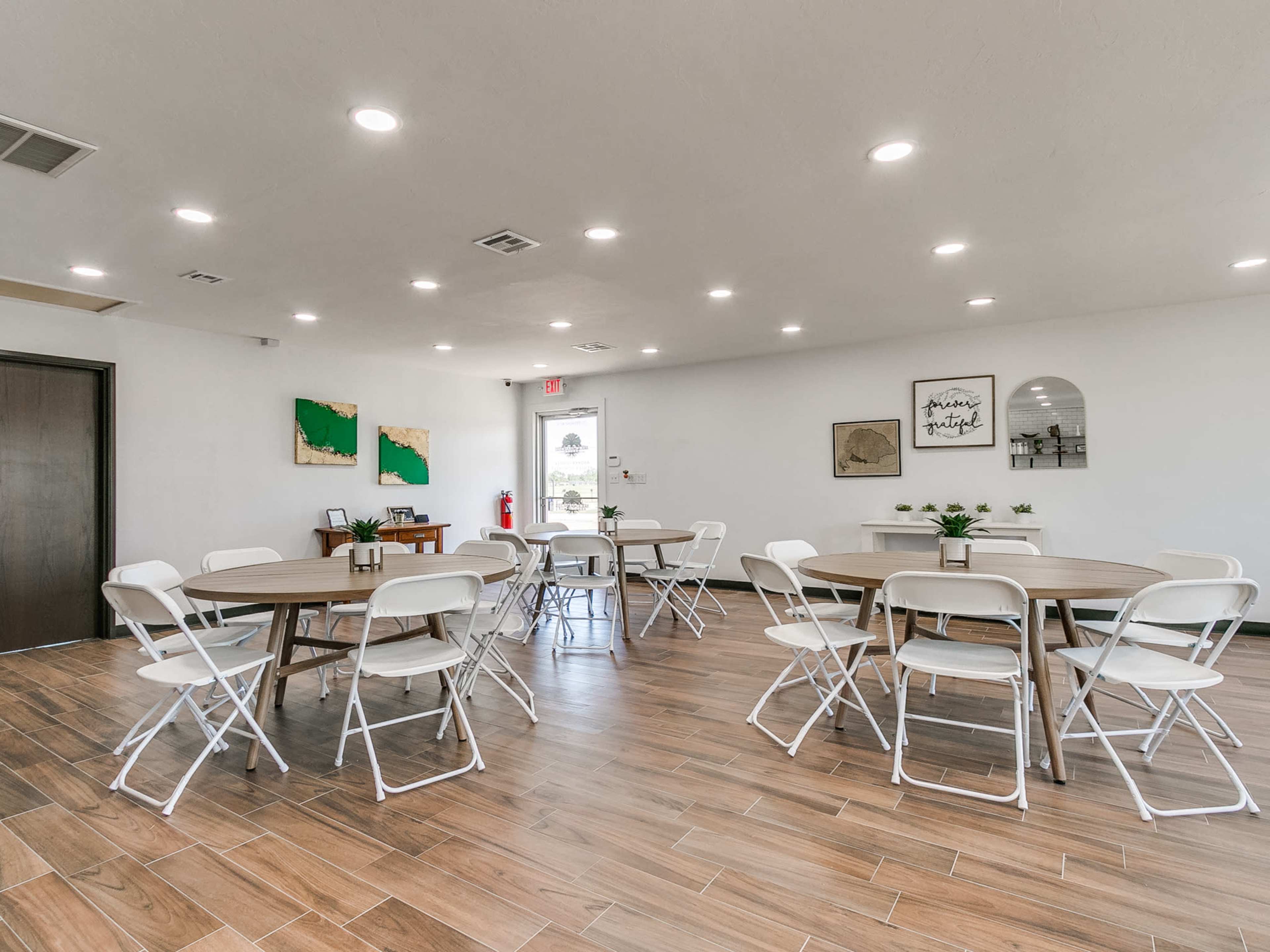 A spacious room with several round tables surrounded by white chairs, decorated with wall art and plants.