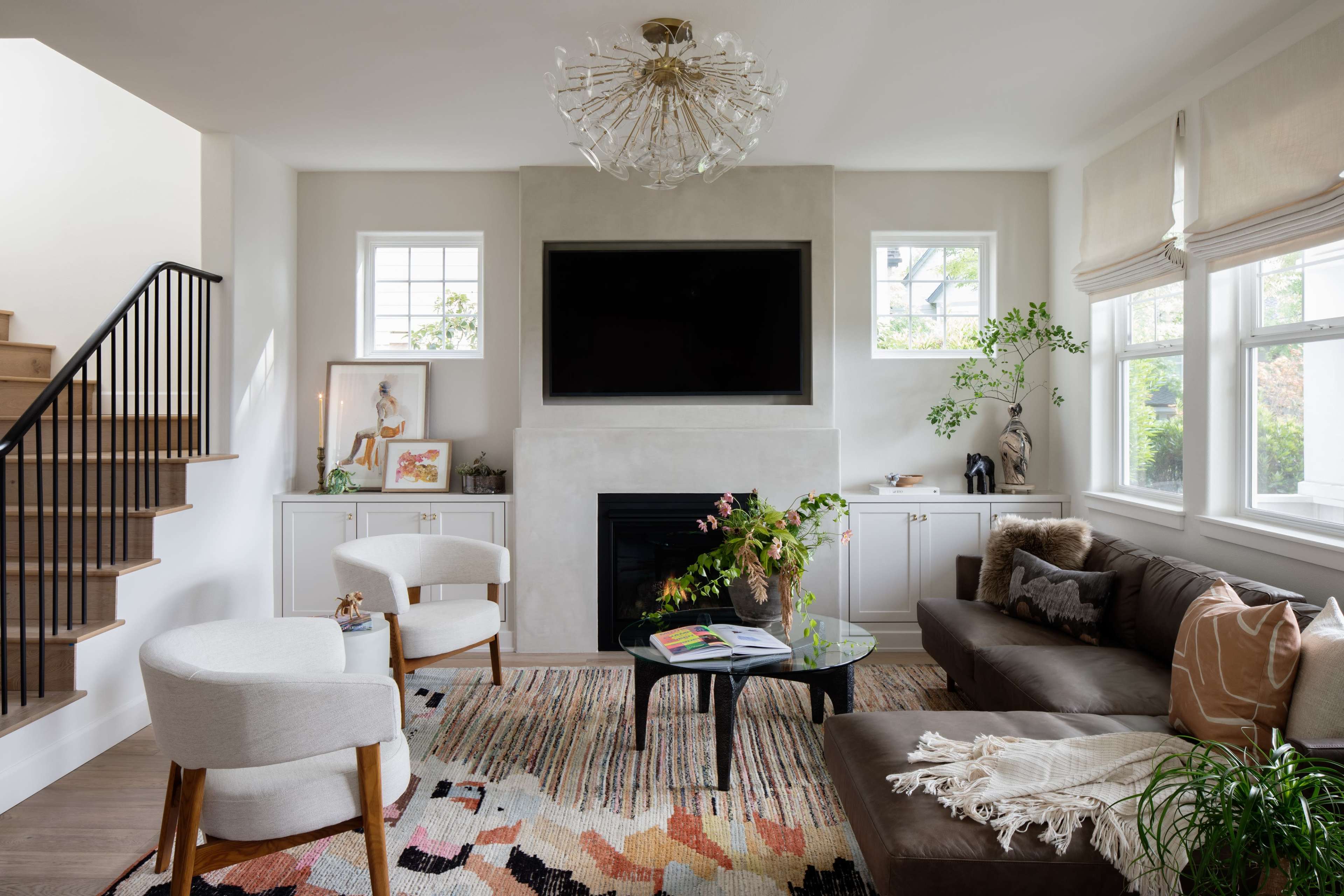 A modern living room features a dark leather sofa, a glass coffee table on a colorful rug, and a sleek fireplace with a mounted television above it.