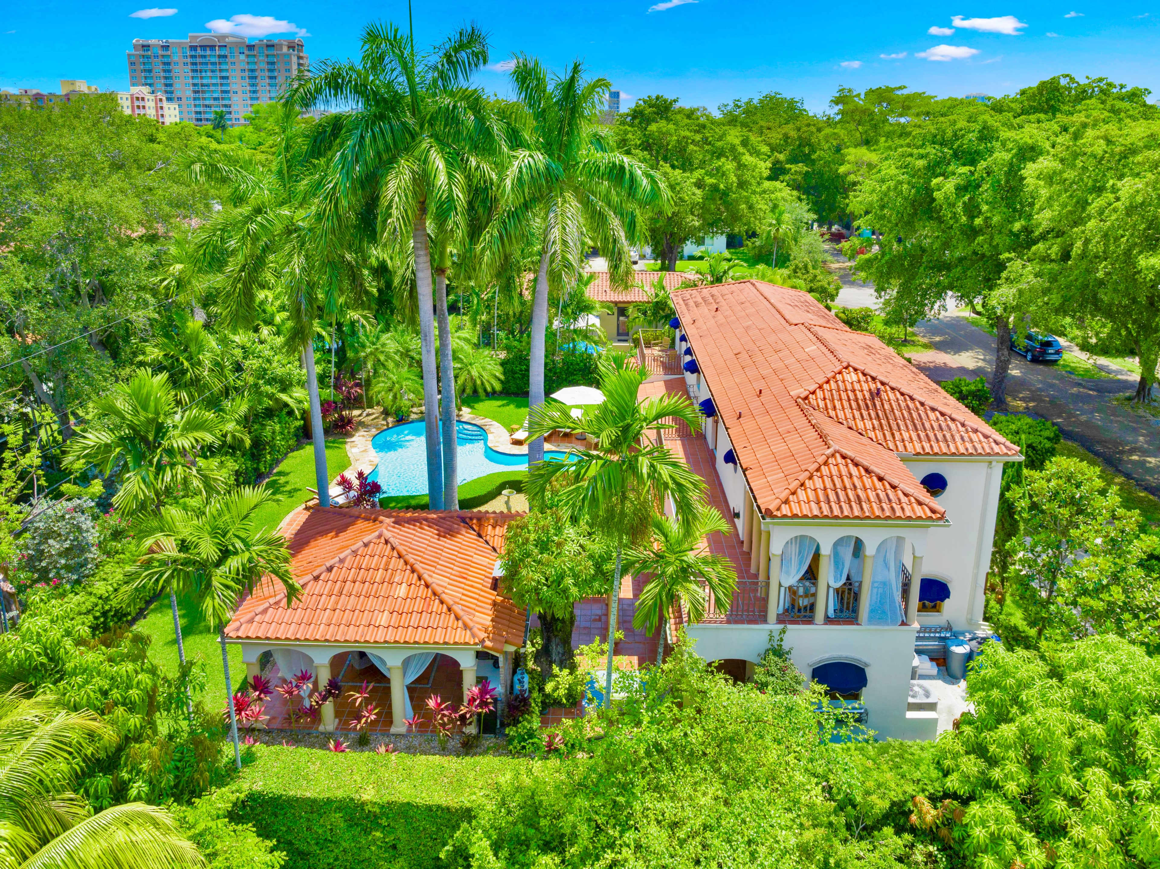 A large residential property featuring a swimming pool, palm trees, and a landscaped yard with various plants and flowers.