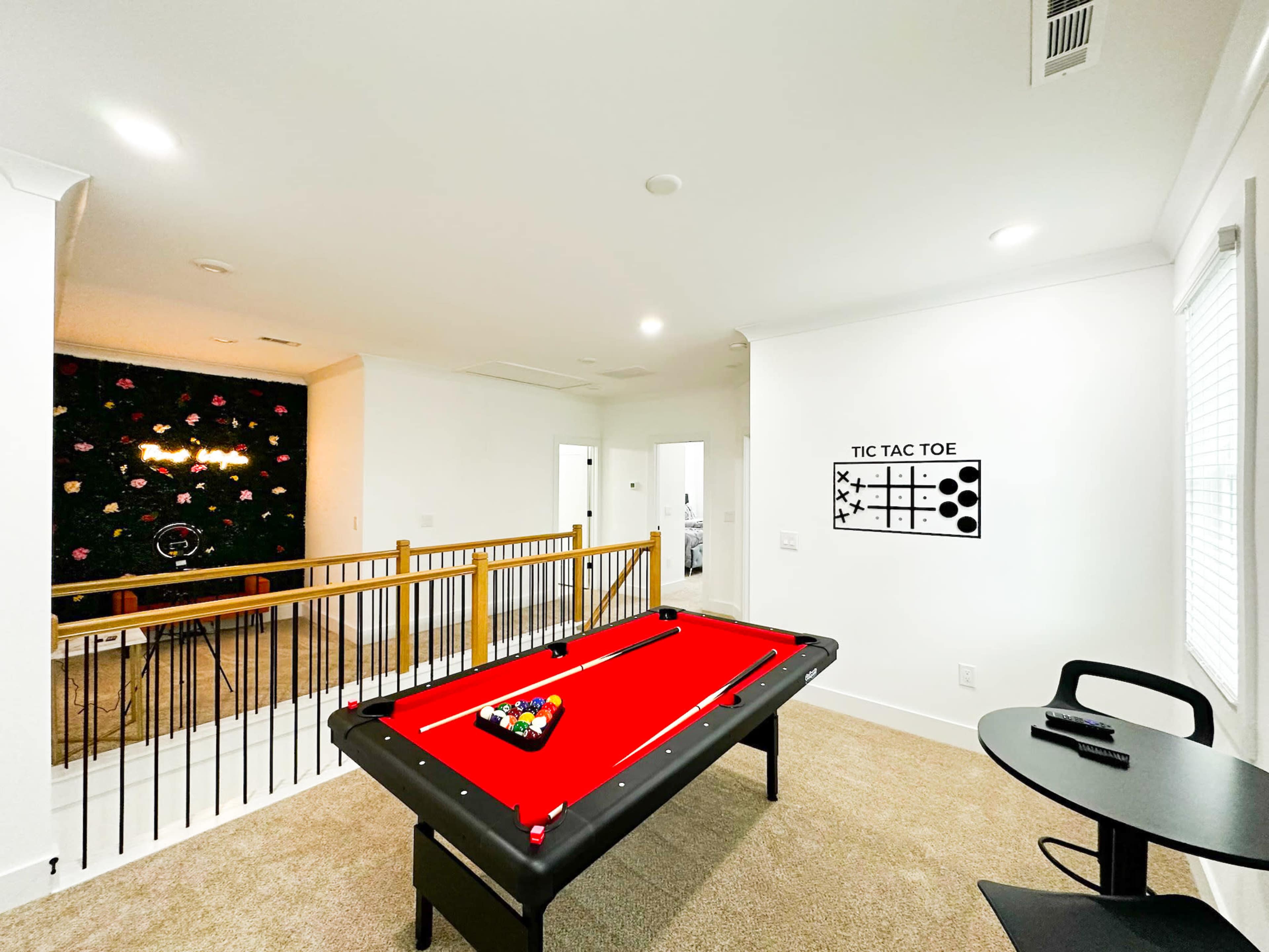 A game room features a red pool table and a tic-tac-toe wall graphic, with a staircase and doorways visible in the background.