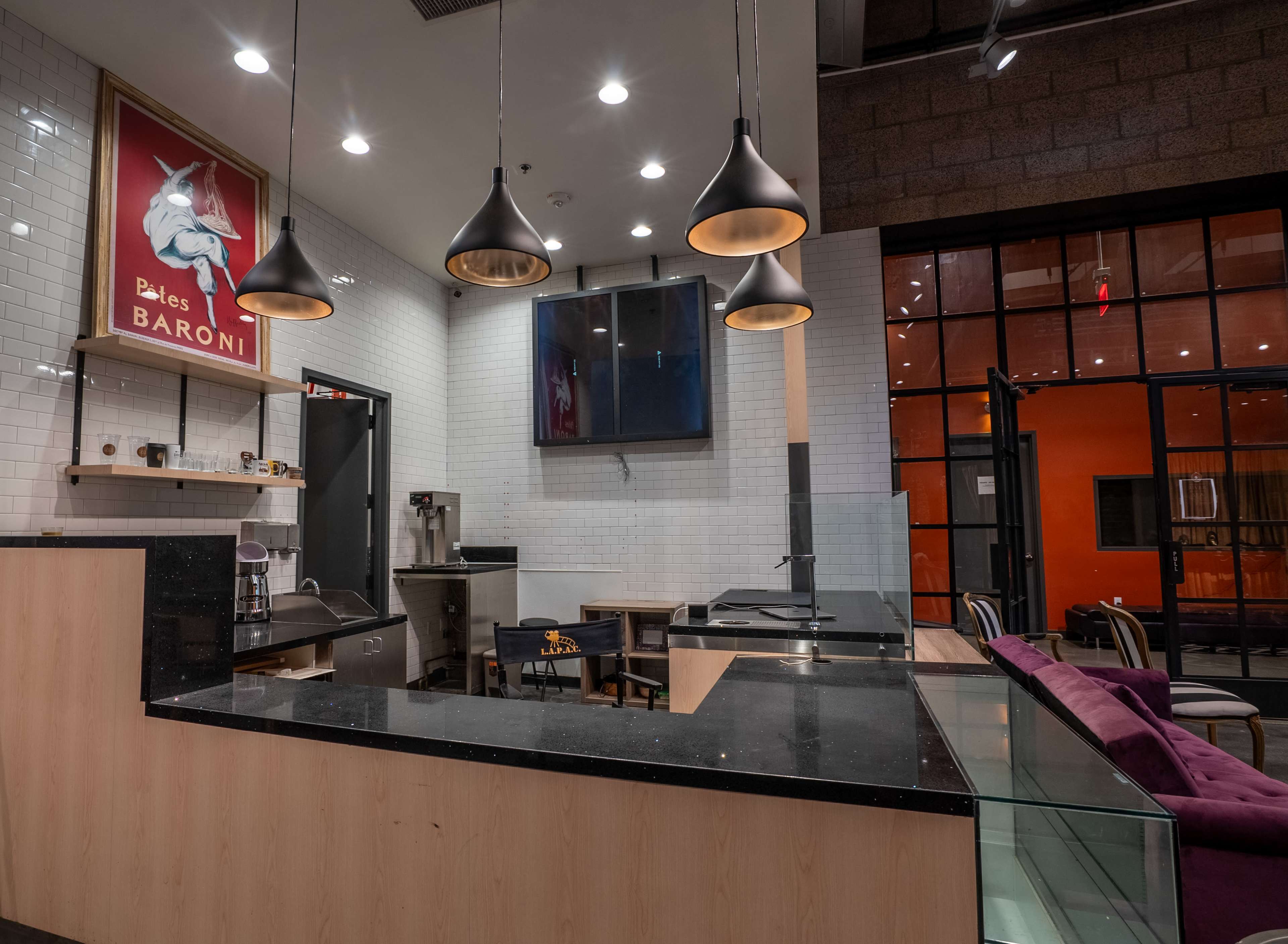 The image shows a modern café interior with a dark counter, a large wall mural of a unicorn, pendant lights hanging from the ceiling, and a cozy seating area visible in the background.