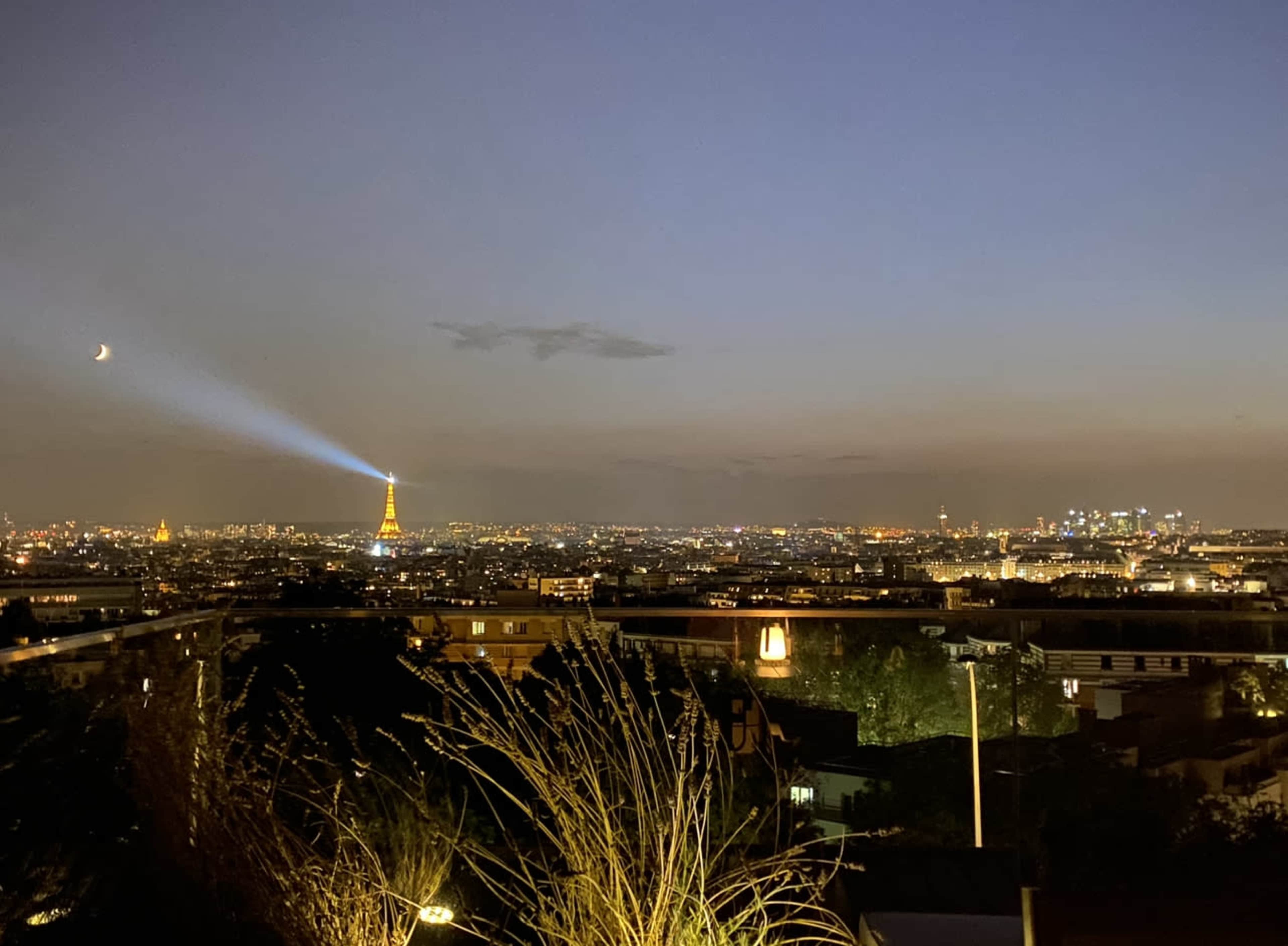 A night view of Paris with the Eiffel Tower illuminated and a beam of light projected into the sky.