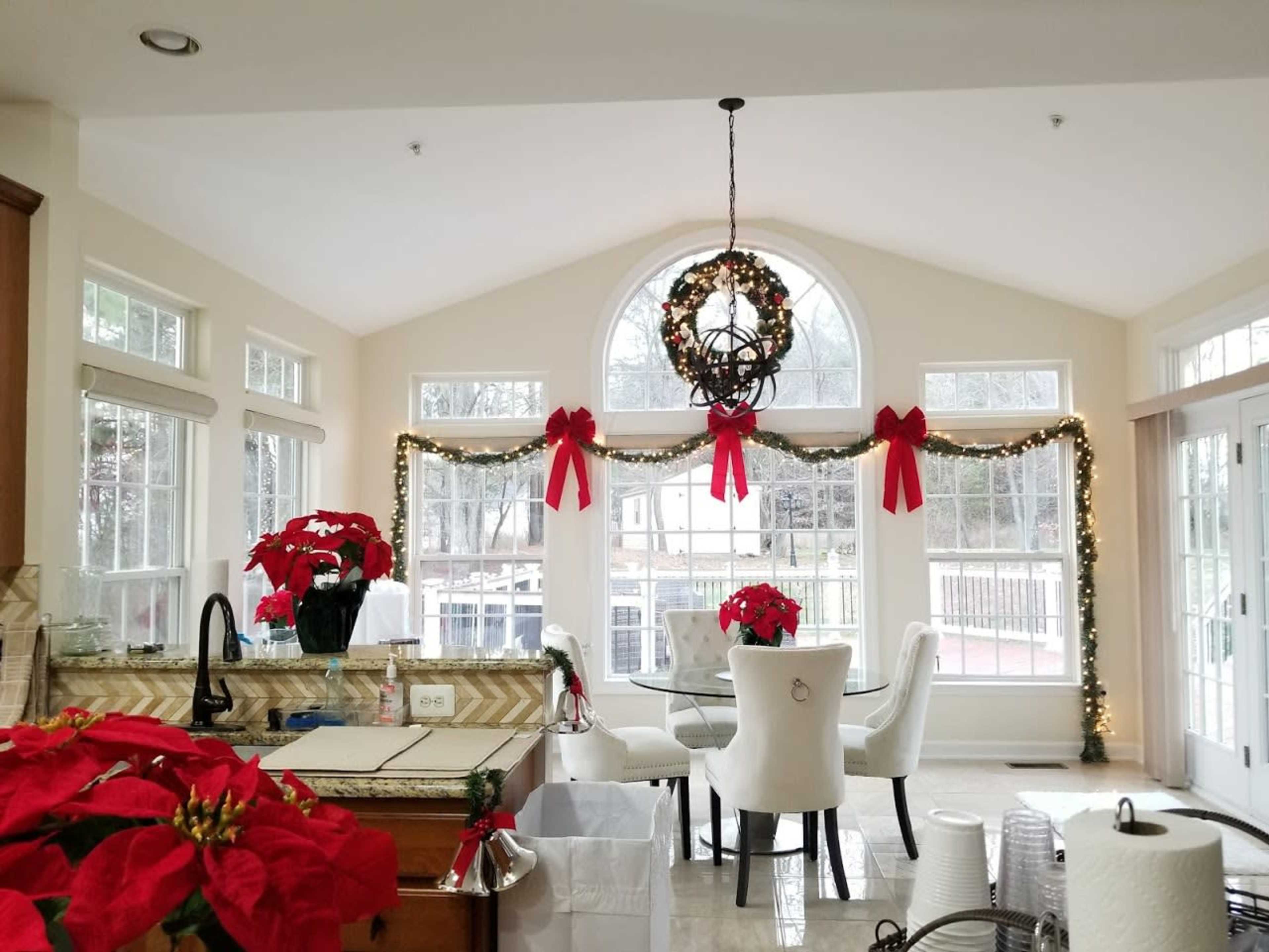 A bright kitchen with holiday decorations, featuring a dining table surrounded by white chairs and adorned with poinsettias.
