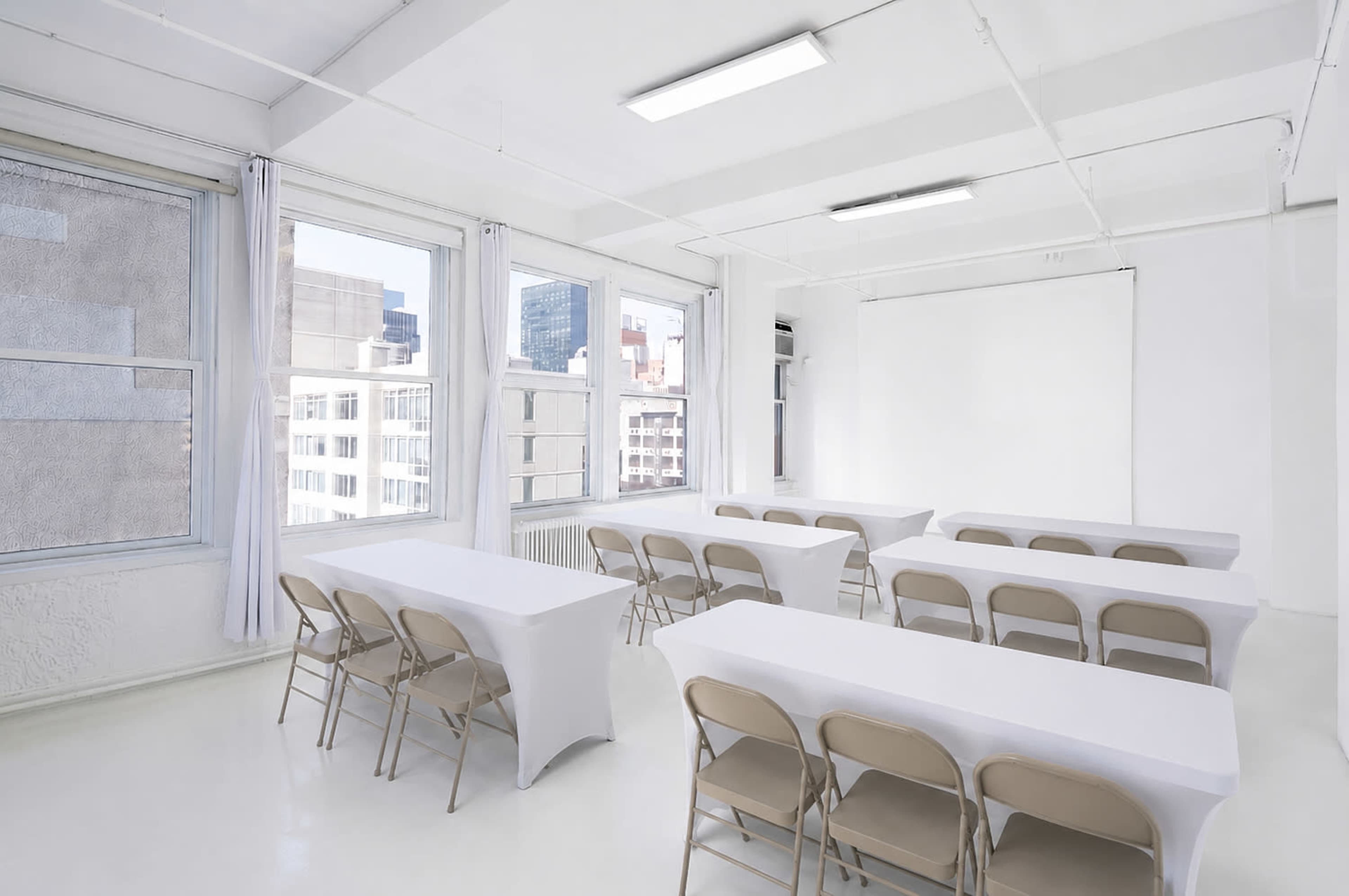 The image shows a bright, modern meeting room with rows of tables and chairs arranged in a clean, white space.