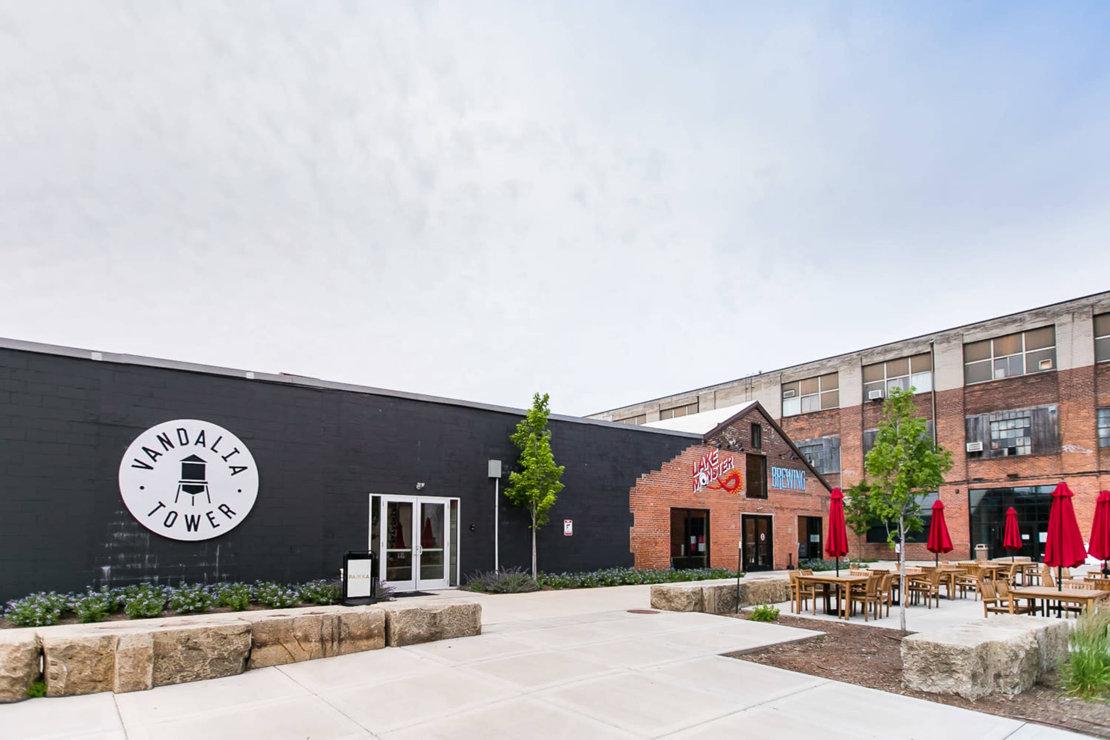 The image shows the exterior of a building labeled "Vandalia Tower," featuring a modern design with outdoor seating and red umbrellas.