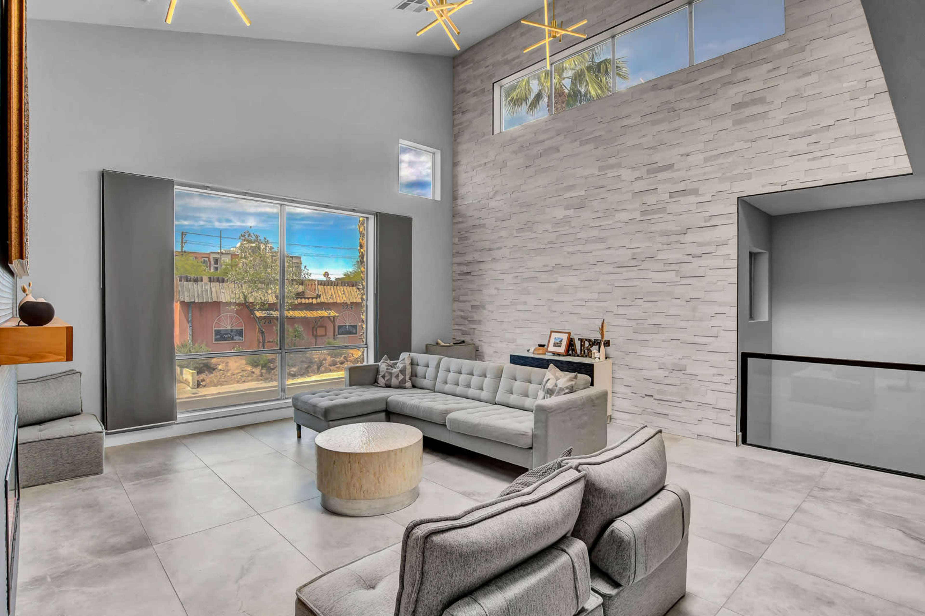 A modern living room features large windows, minimalist furniture, and a textured stone wall.
