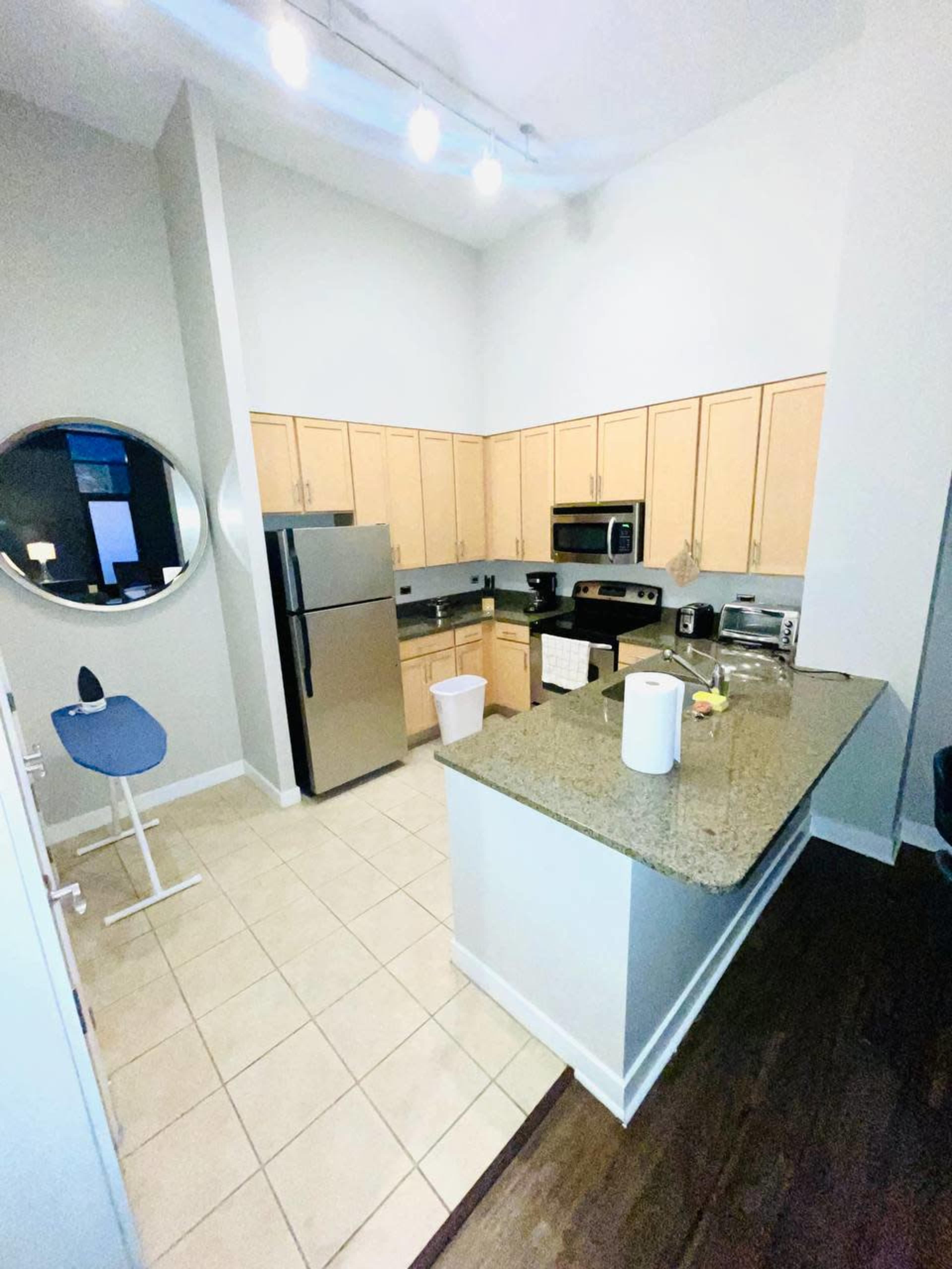 A modern kitchen layout featuring light wood cabinets, stainless steel appliances, and a central island with a granite countertop.