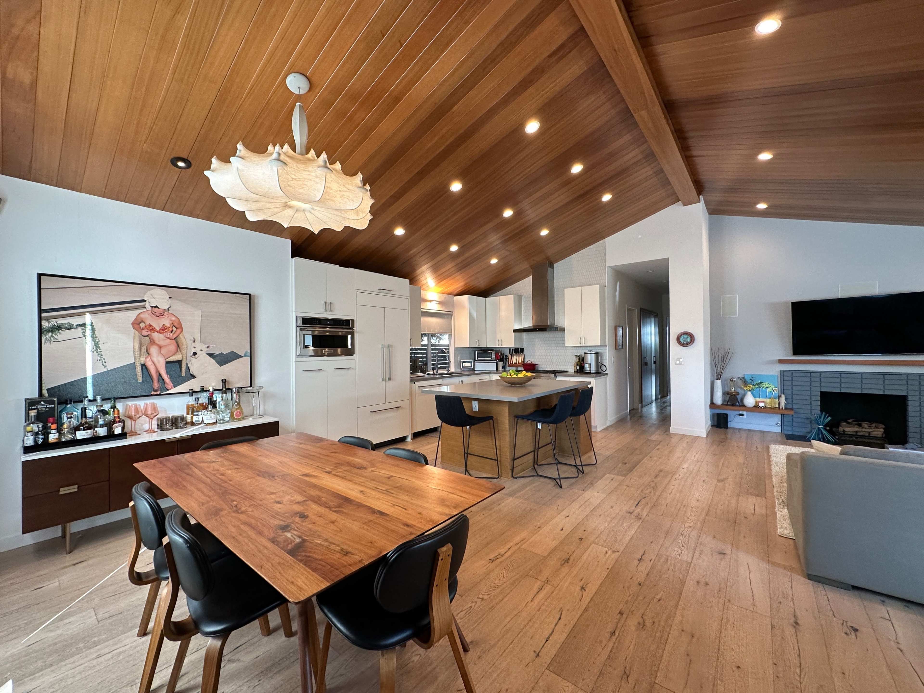 A modern kitchen and dining area with wooden ceilings, a large table, and a television displaying a framed photo.