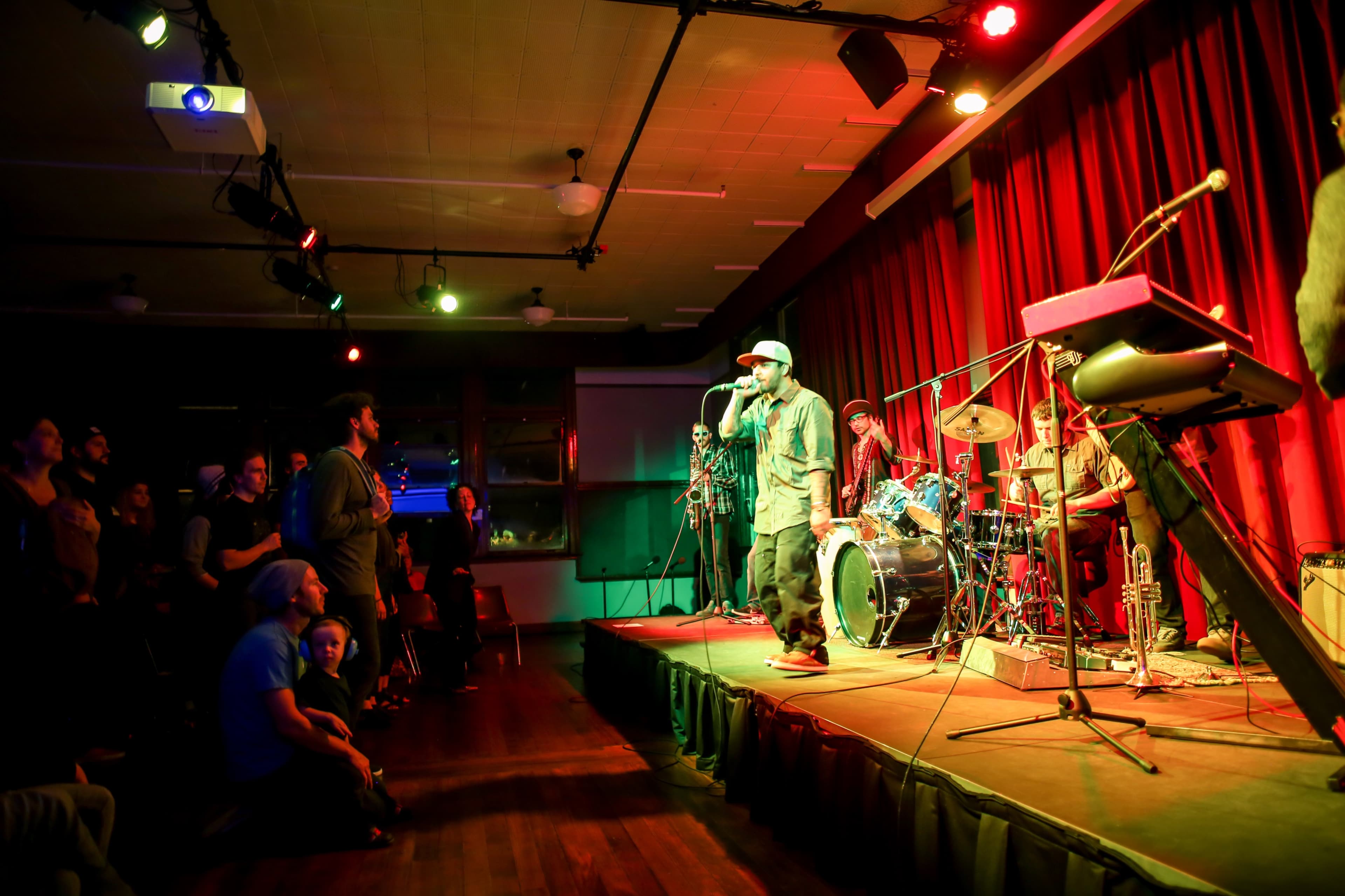 A performer raps on stage while a band plays behind him and an audience watches from below.