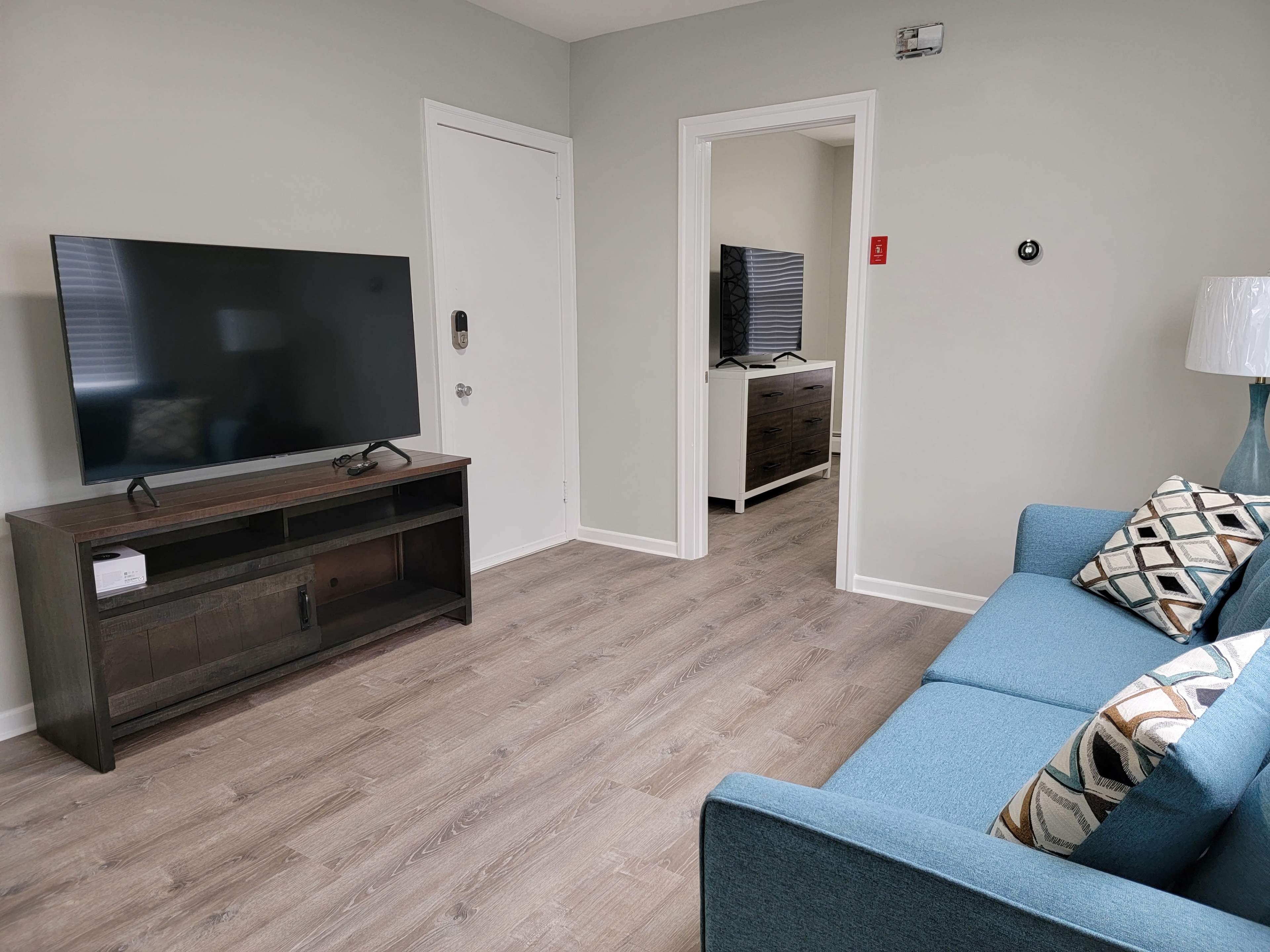 A living room features a blue sofa, a television on a wooden stand, and an open doorway leading to another room.
