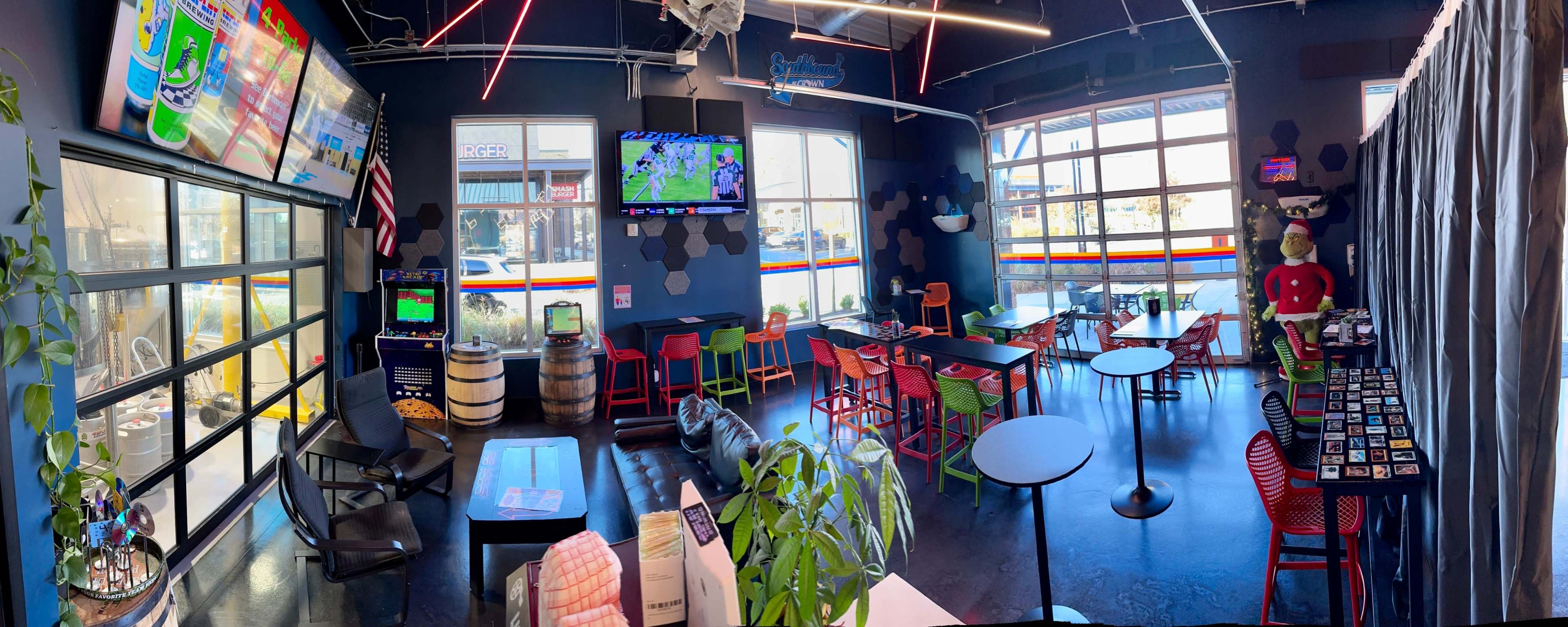 A spacious sports-themed bar with colorful seating, multiple televisions displaying a game, and large windows allowing natural light to enter.