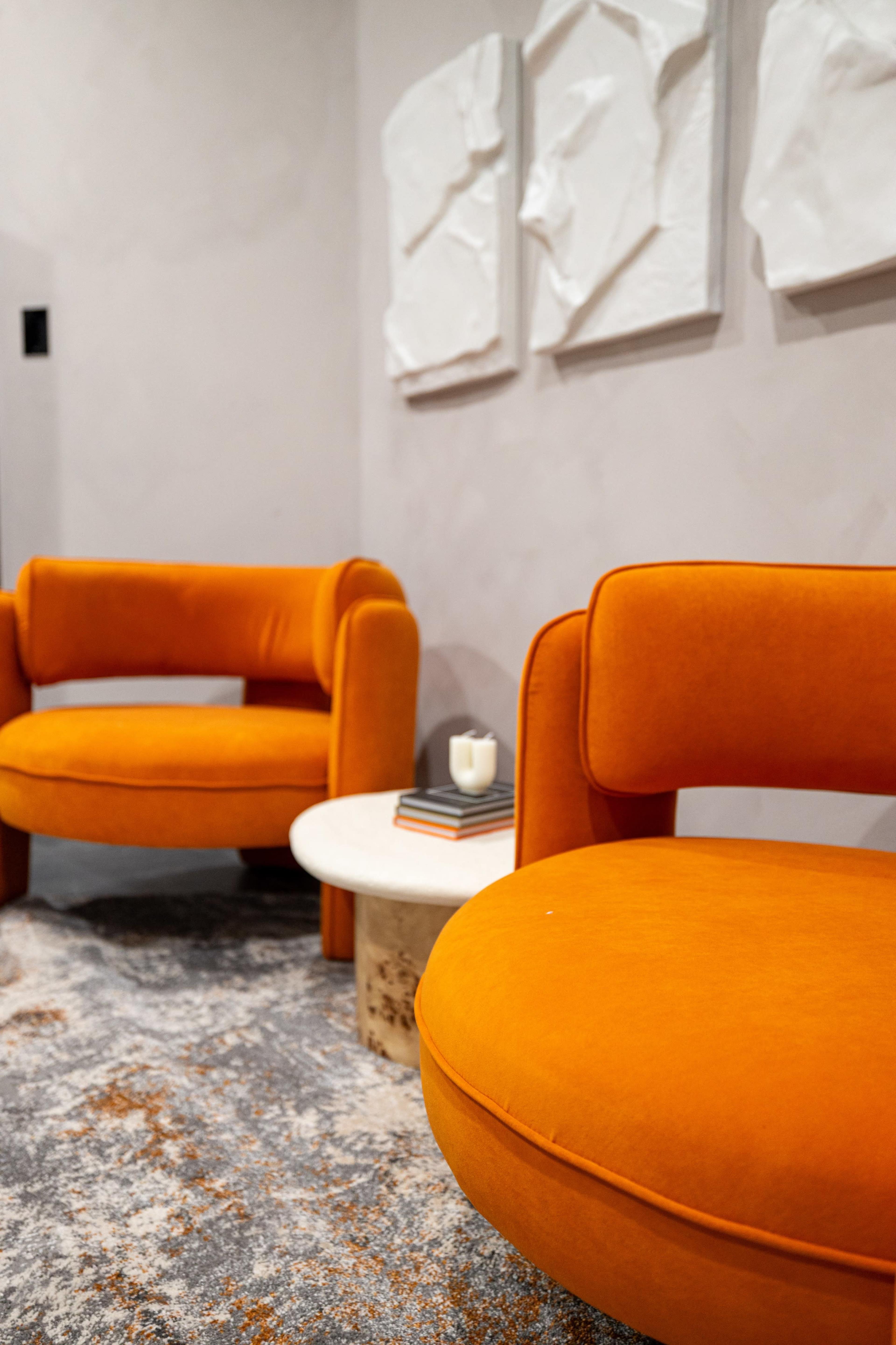 A small seating area with two orange, rounded chairs and a round white table on a textured rug.