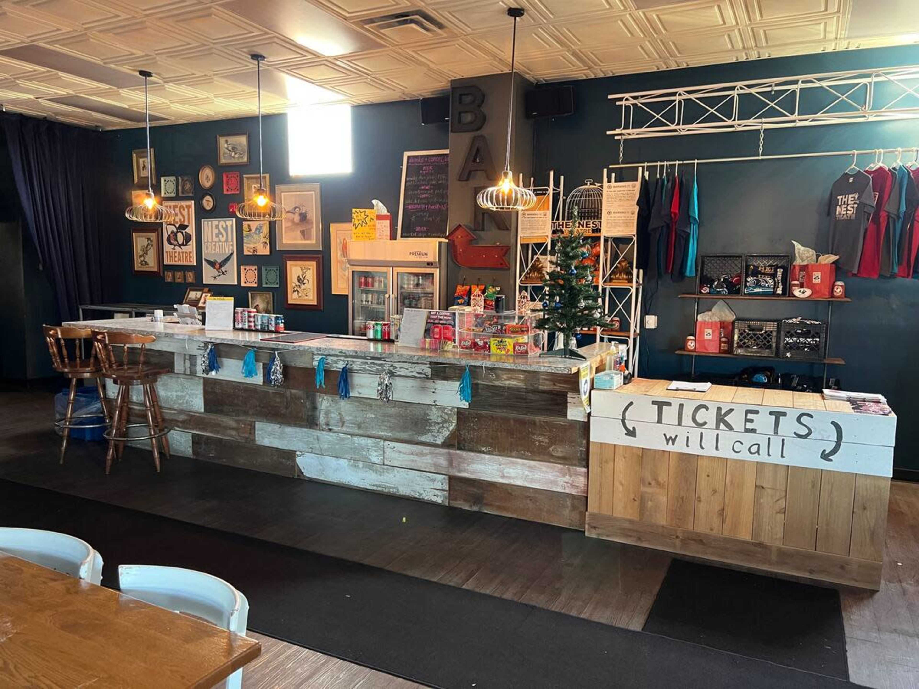 A ticket counter and a concession area set up inside a venue, featuring wooden counters, colorful merchandise displays, and decor on the walls.