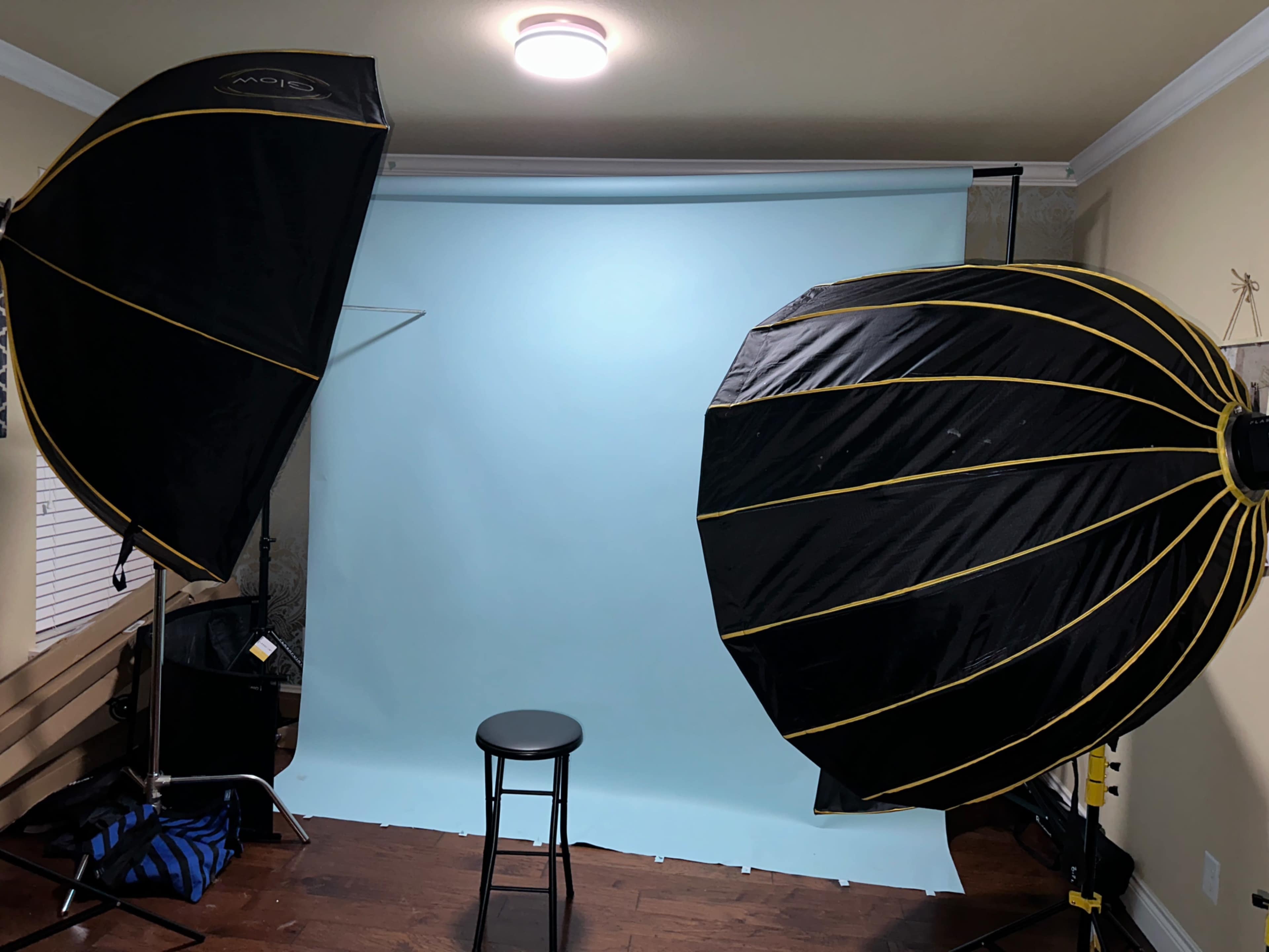 The image shows a photography setup with two large softbox lights positioned on either side of a blue backdrop and a black stool in the center.