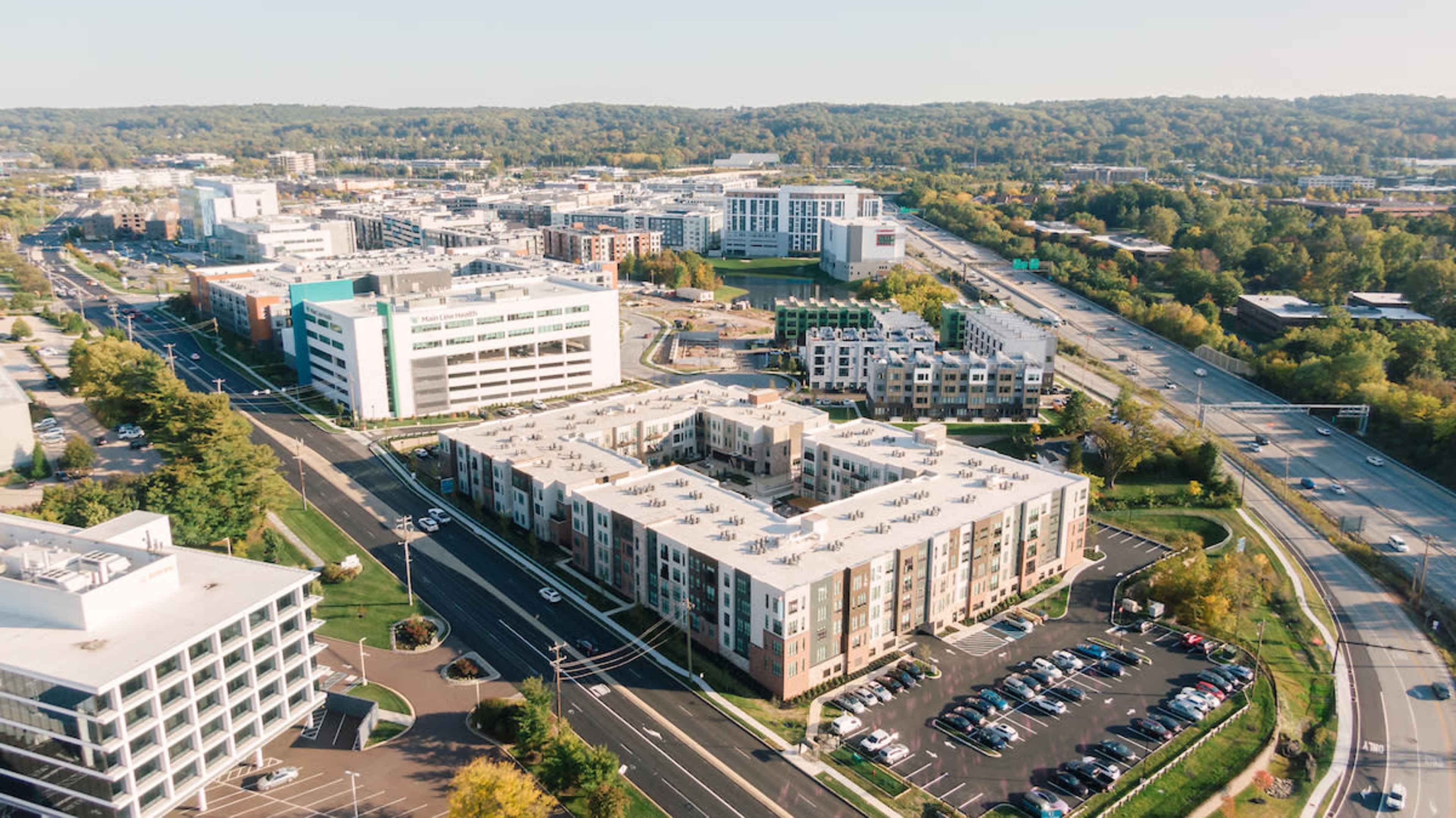 The image shows an aerial view of a modern urban area featuring residential and commercial buildings, green spaces, and roadways.