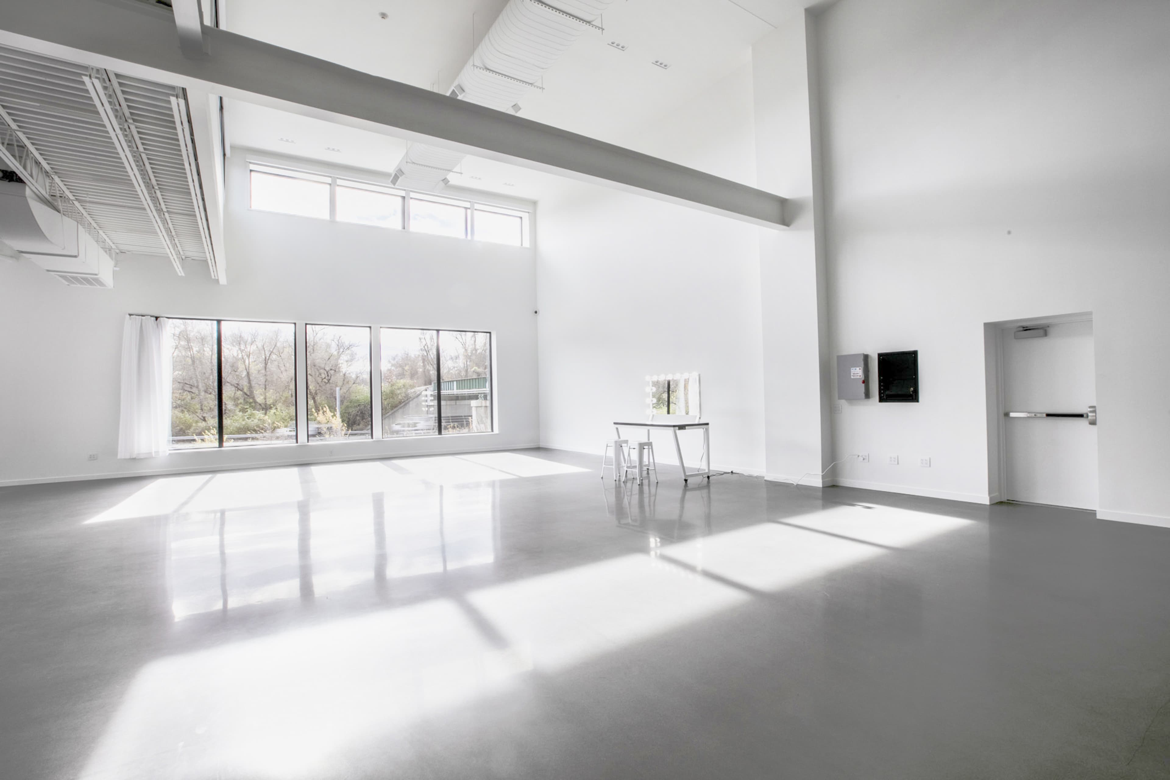 A spacious, empty room with large windows allowing natural light to illuminate the polished concrete floor and minimal furnishings.