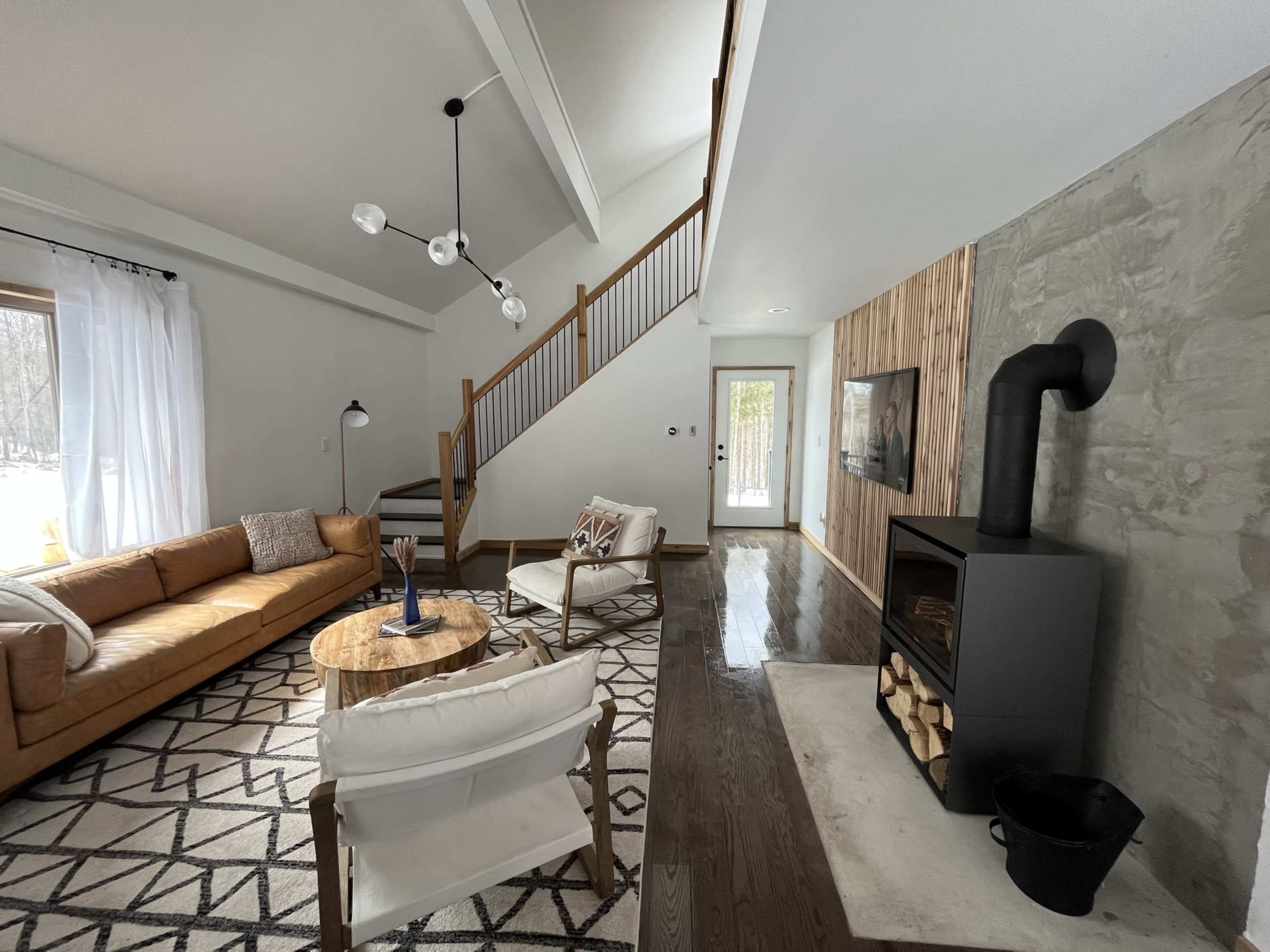 A modern living room with a leather sofa, a round wooden coffee table, and a black fireplace, featuring high ceilings and large windows.