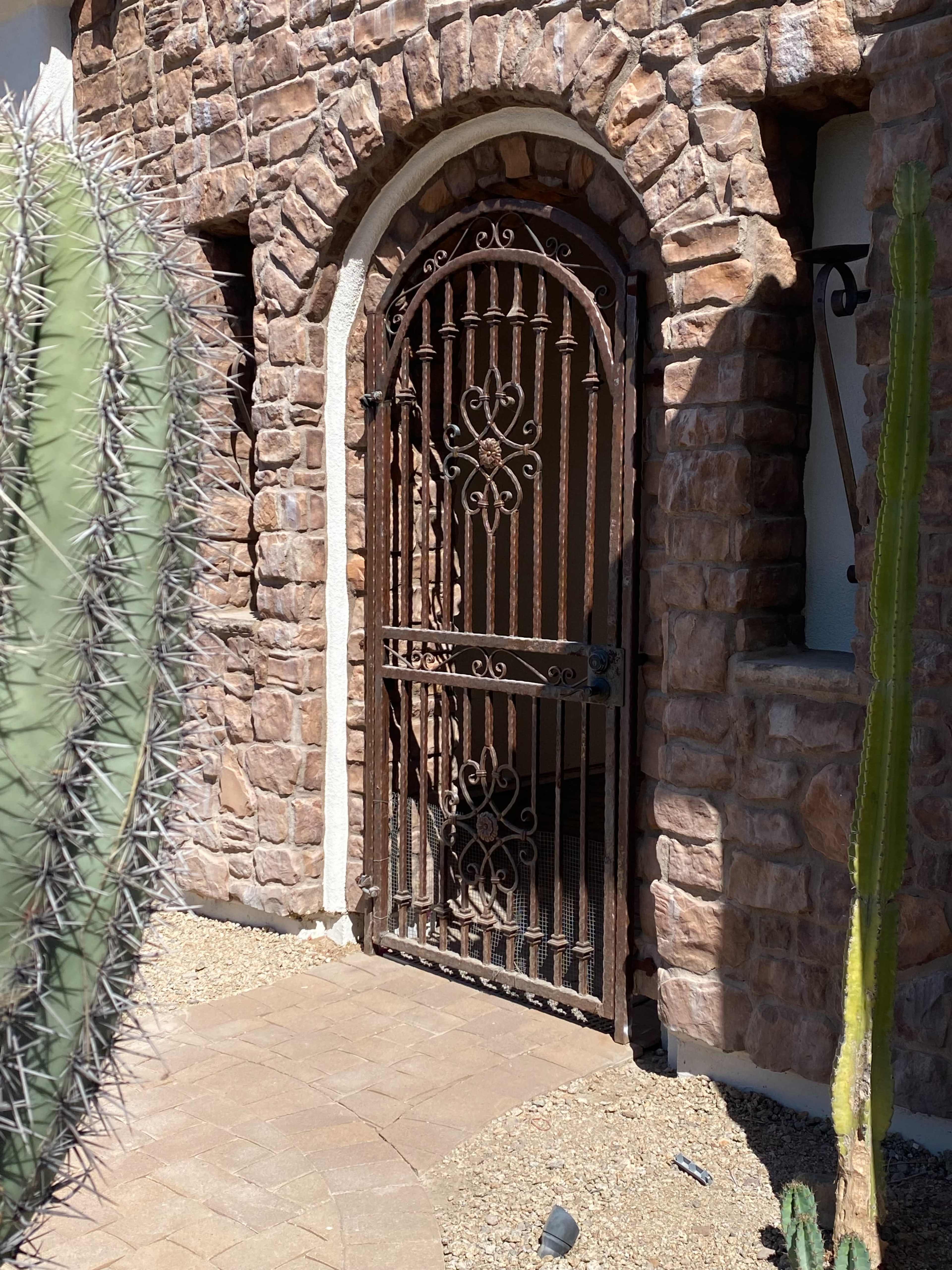 A wrought iron gate is set into a stone wall, surrounded by a cacti garden.