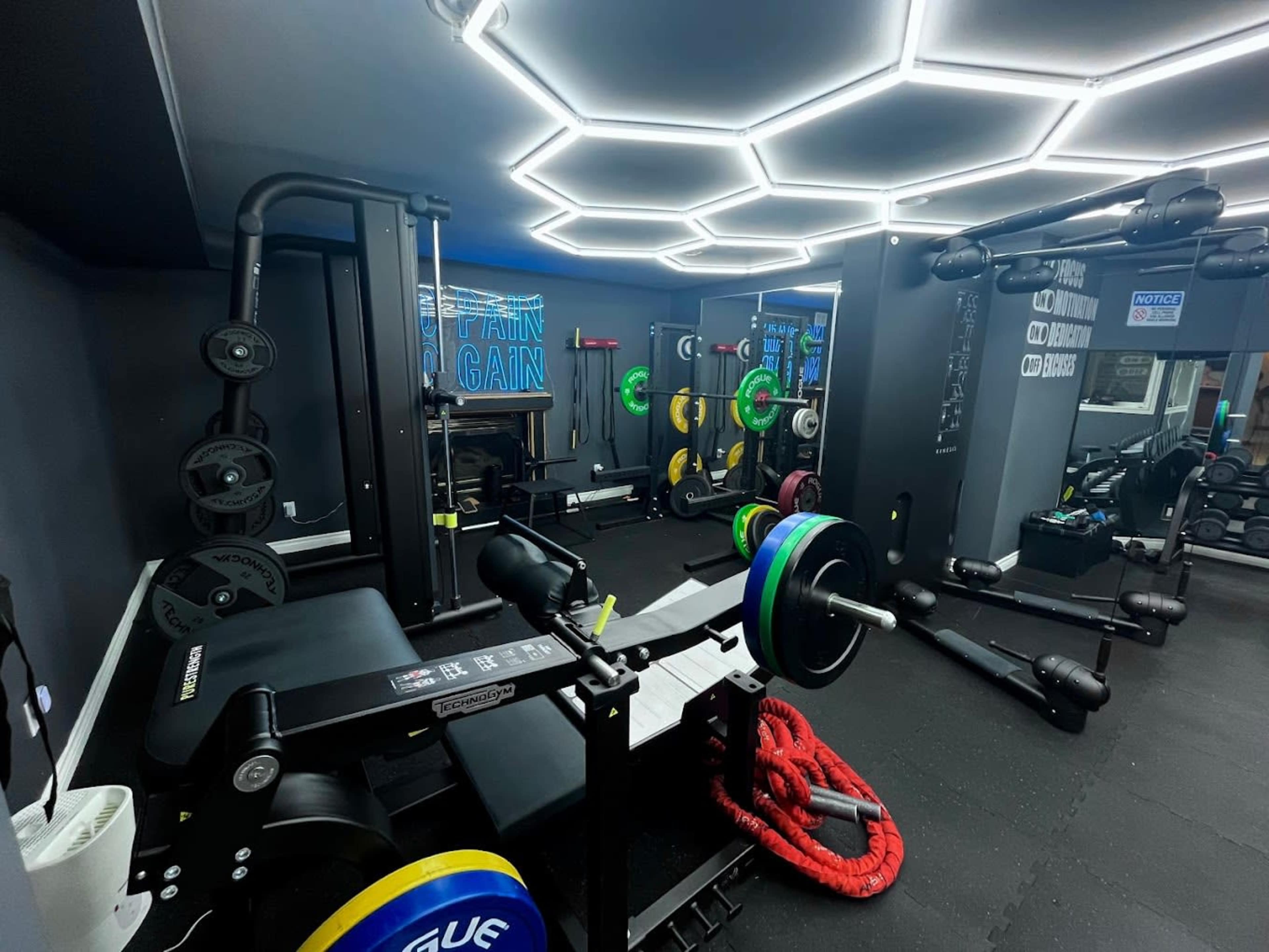 A modern gym interior with various weightlifting equipment, including a bench press and free weights, illuminated by hexagonal LED lights.