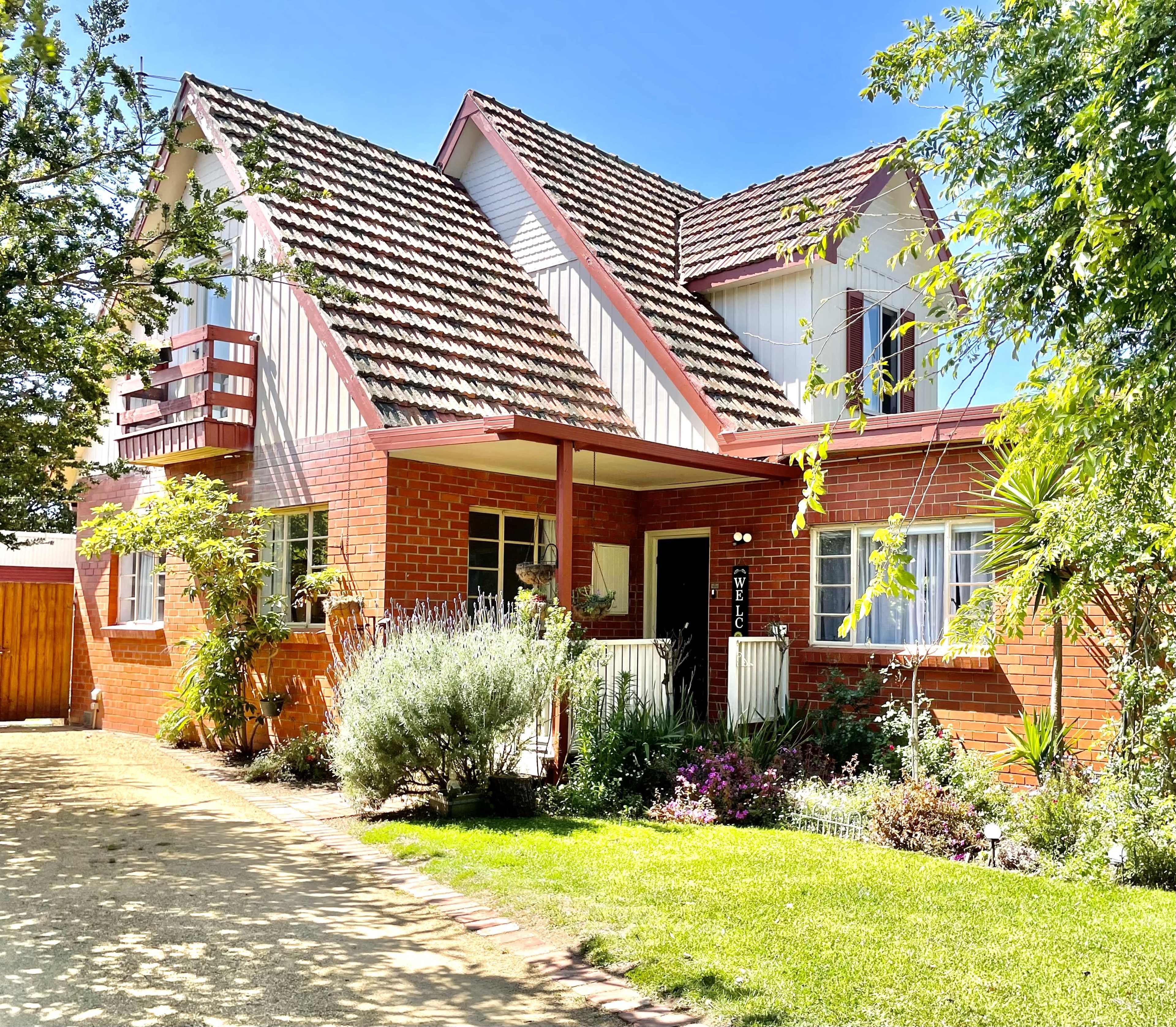 A red-brick house with a steeply pitched roof and a landscaped front yard is situated on a gravel path.