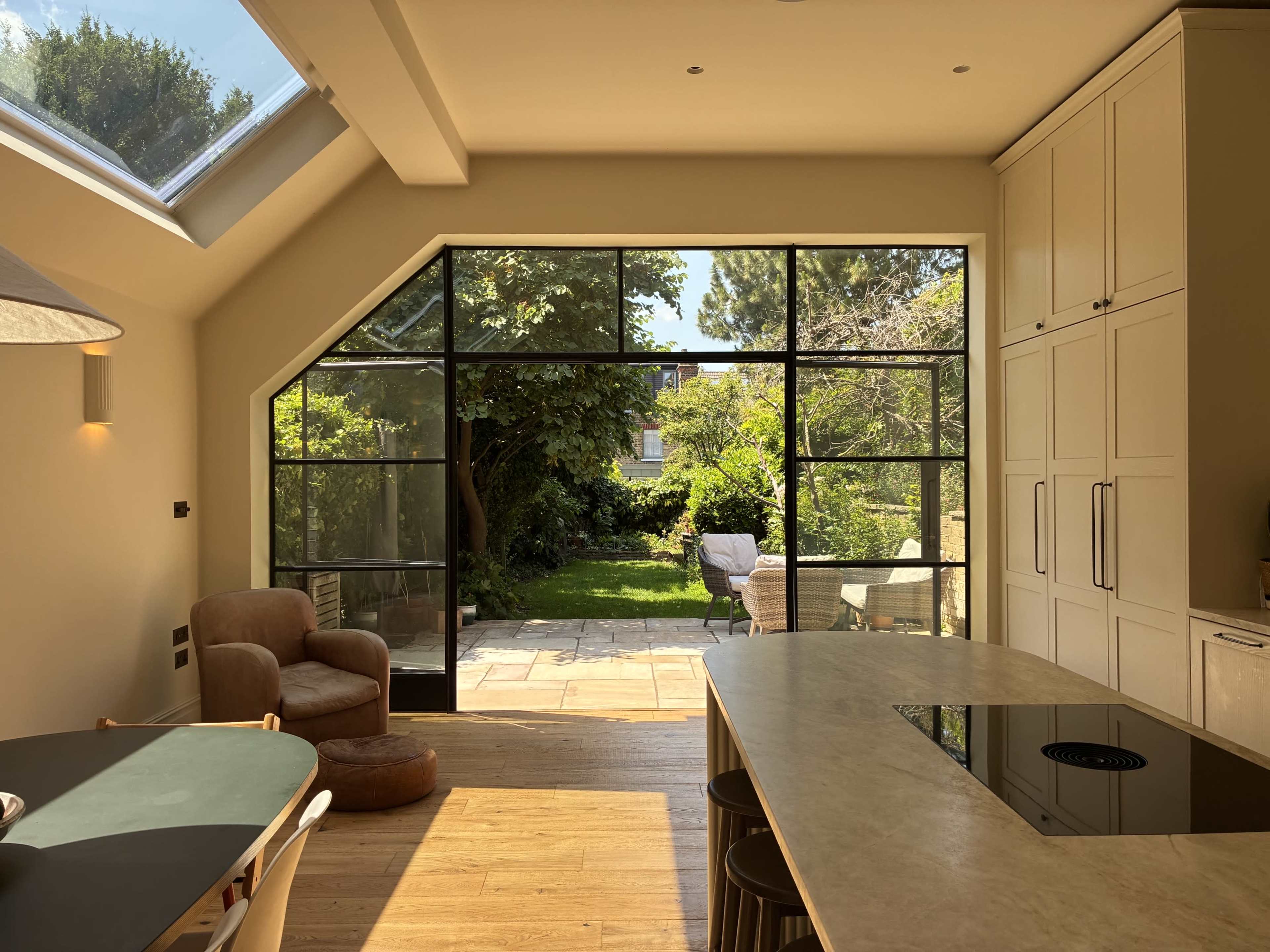 The image shows a modern kitchen with a large glass door leading to a lush garden area.