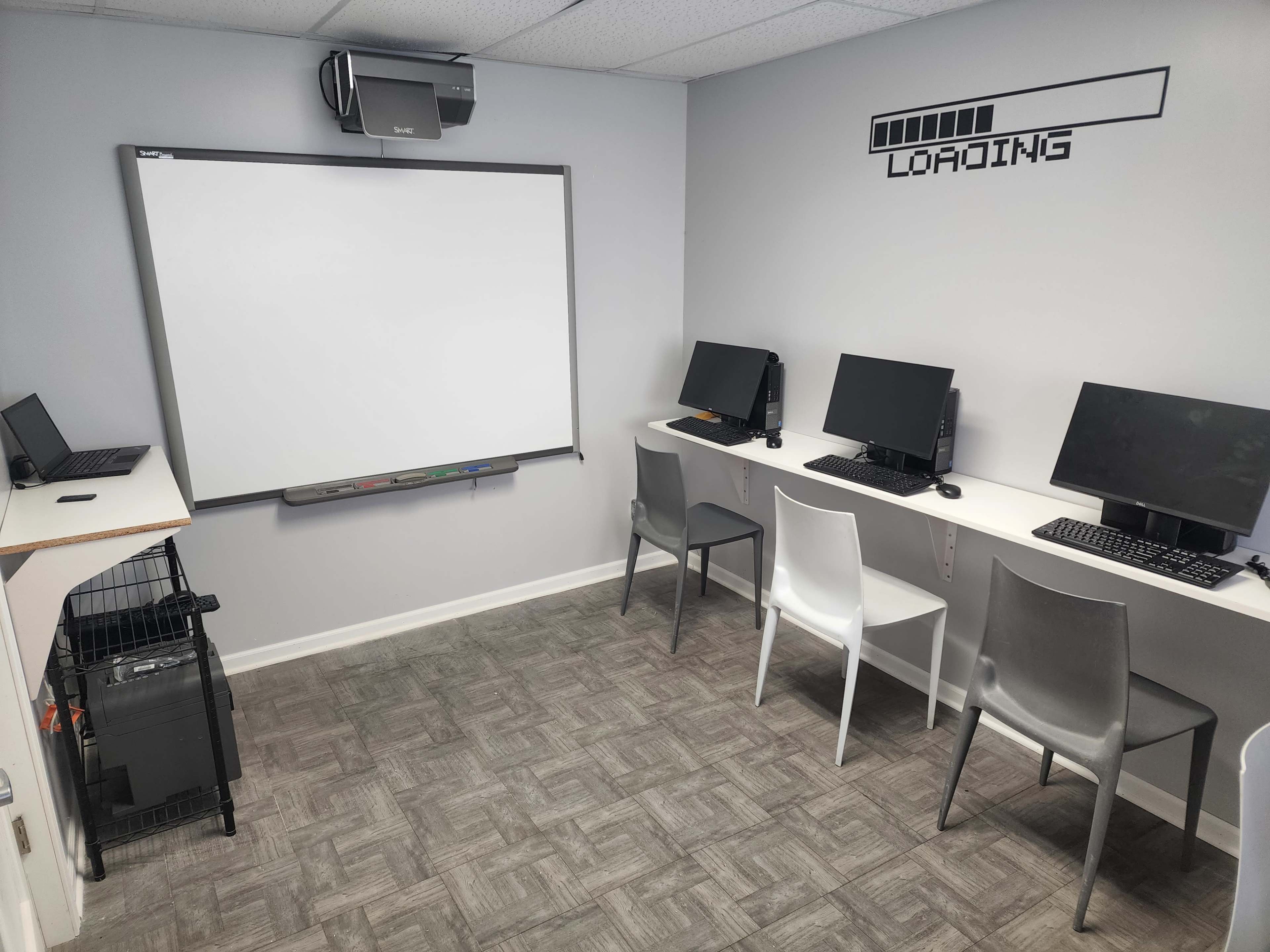 A small computer room with four desktop computers, a blank whiteboard, and a projector mounted on the ceiling.
