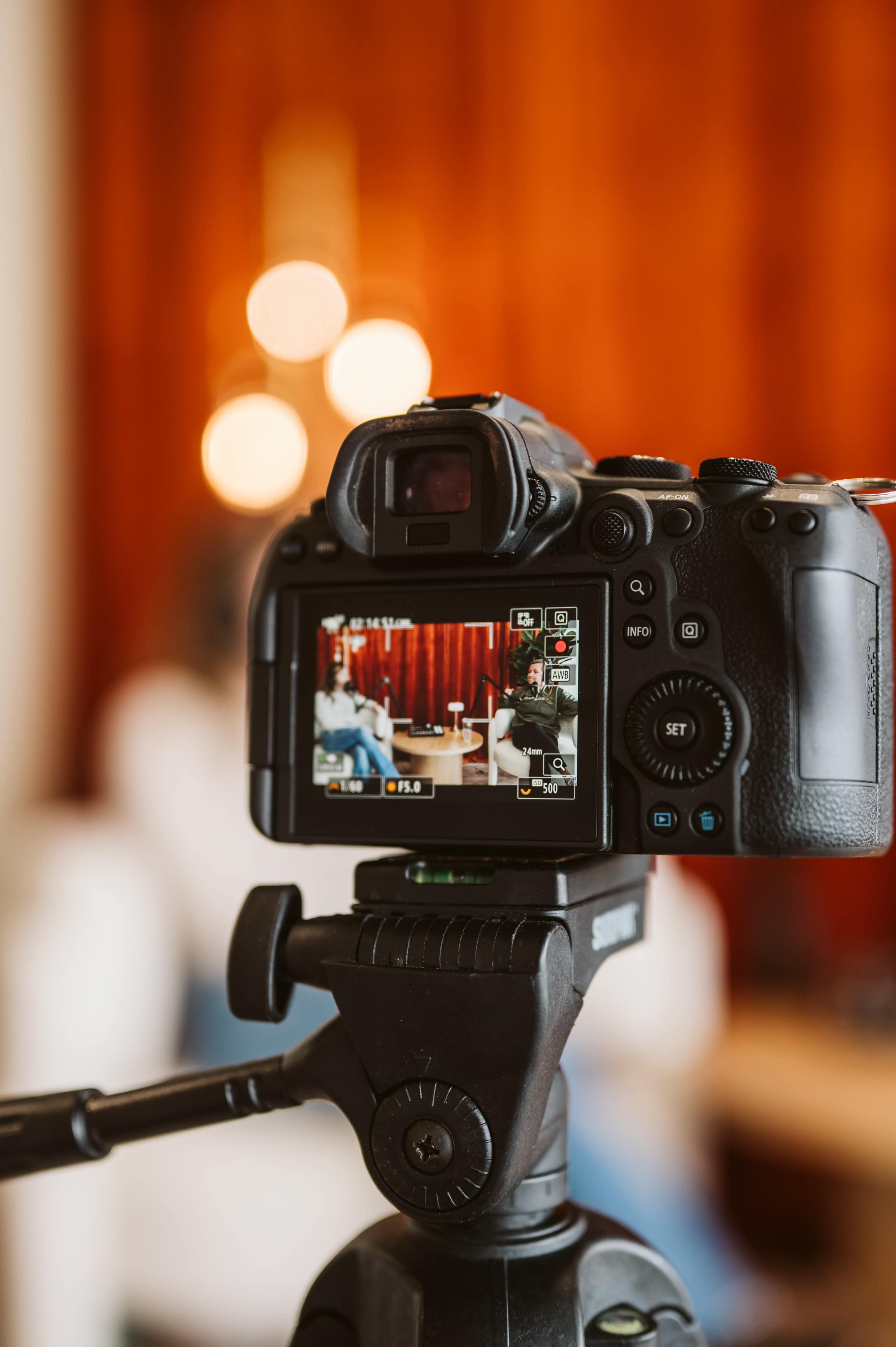 A camera on a tripod is focused on a seated subject with a blurred background of warm colors.
