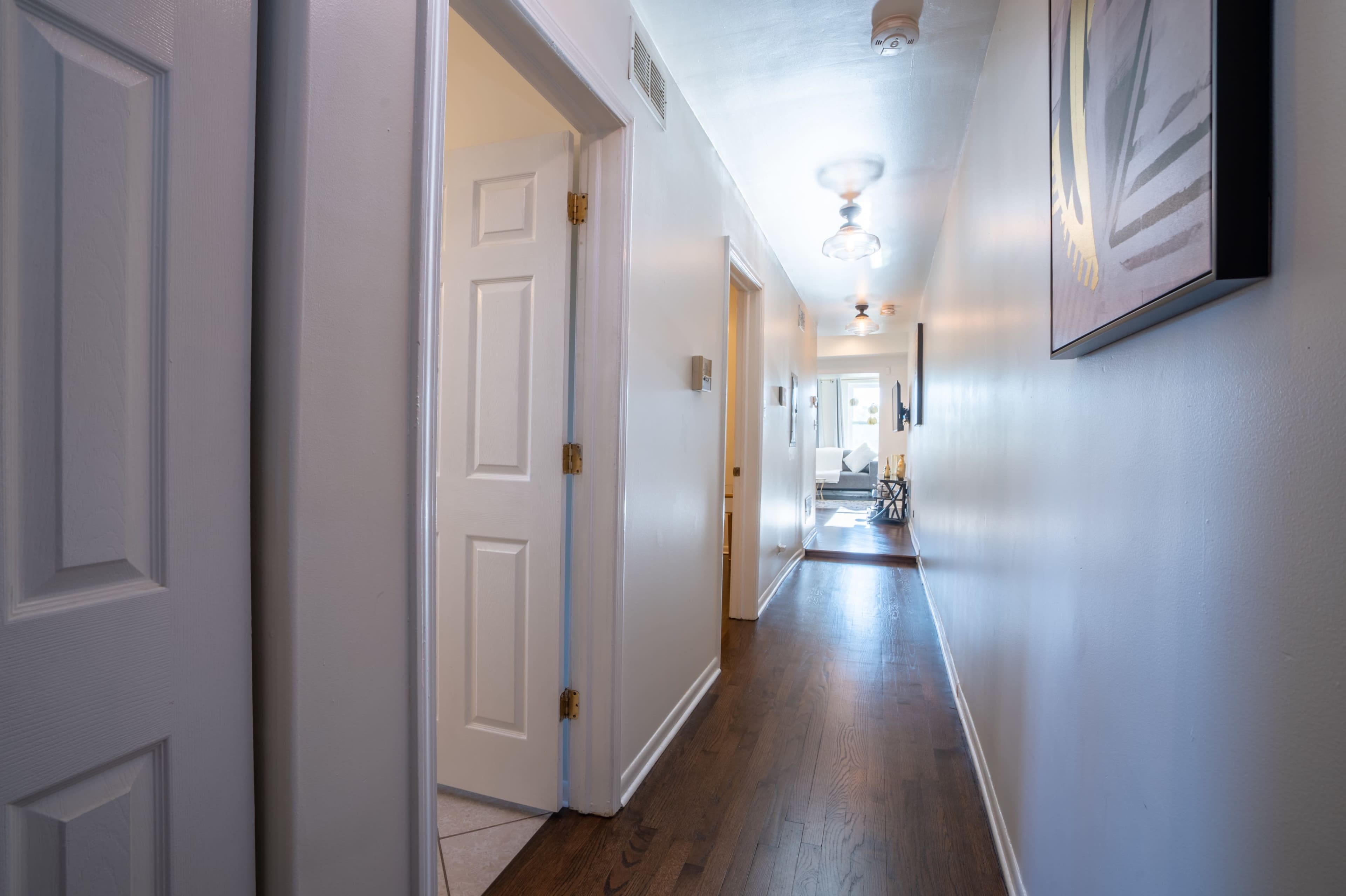A narrow hallway with doors on either side leads to a brightly lit room at the end.