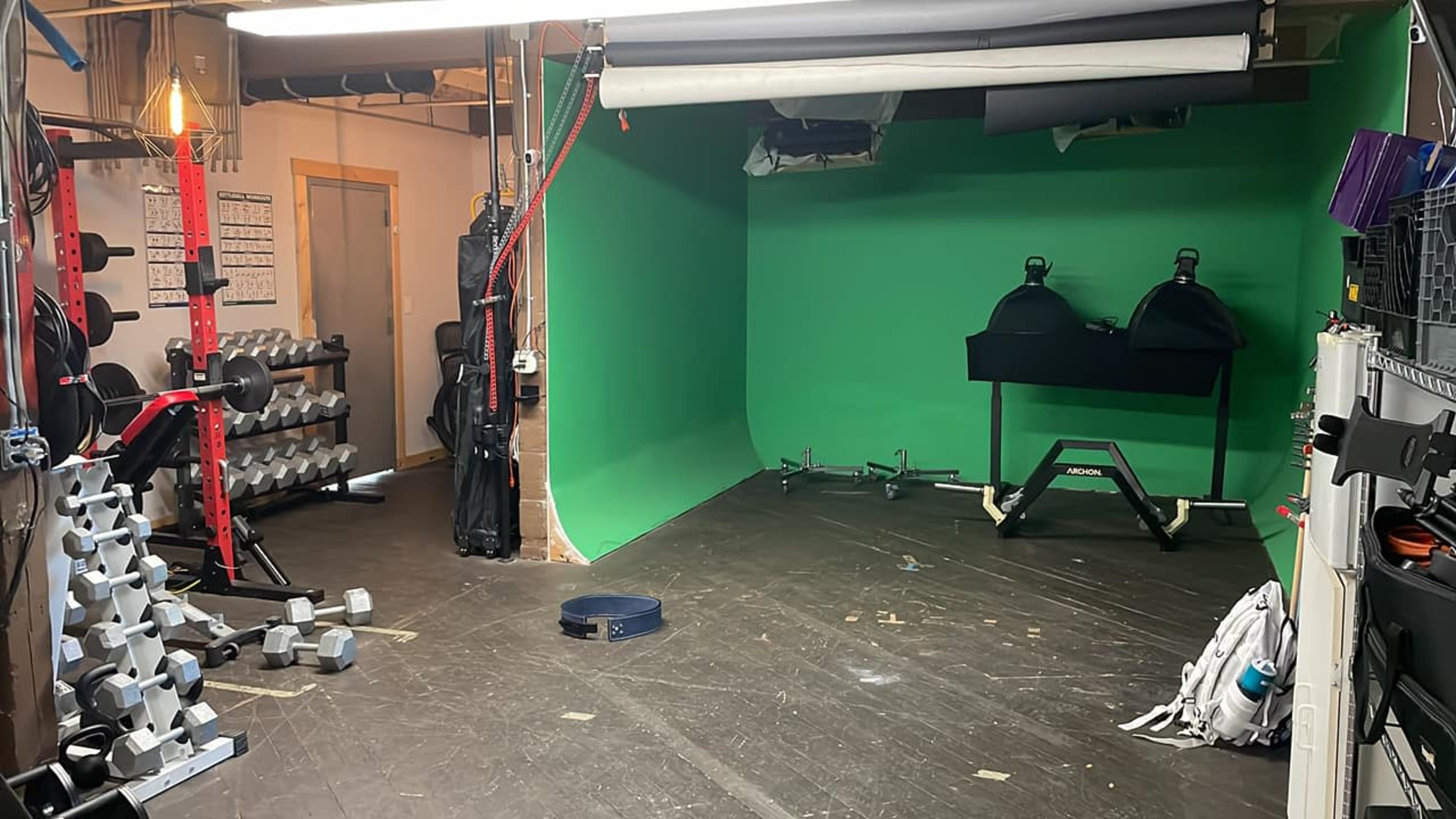 A gym space featuring weightlifting equipment, a green backdrop, and a black cart on wheels.