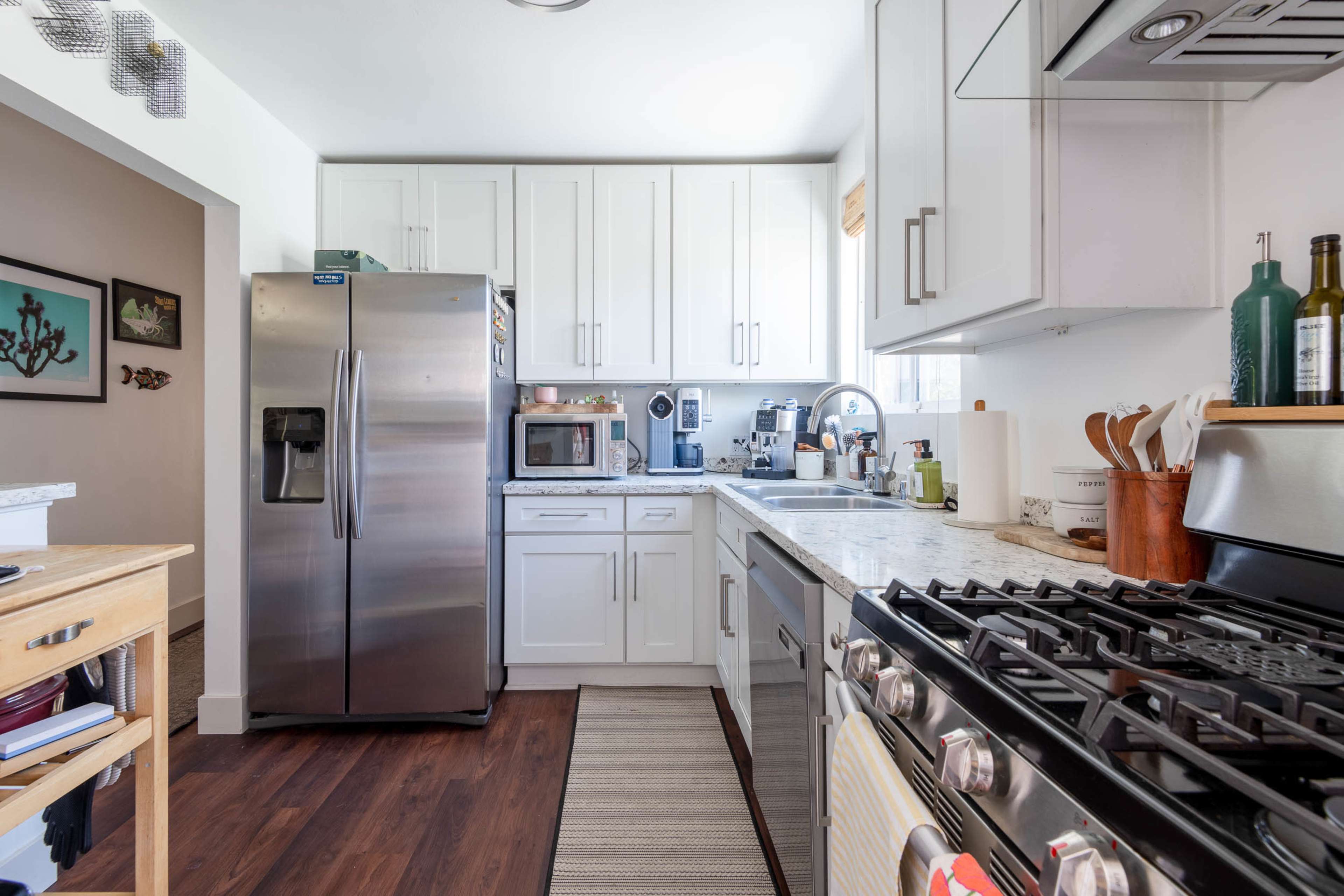 The image shows a modern kitchen with white cabinets, stainless steel appliances, and a gas stove, featuring a clean and organized layout.